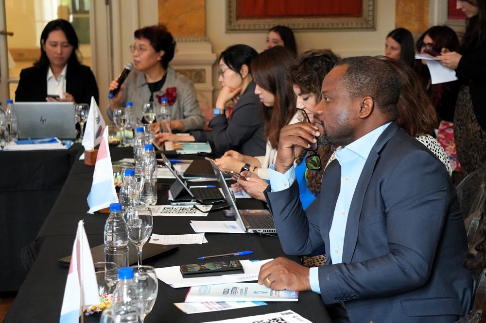 Man in blue suit at the right foreground during a business meeting with delegates and laptops.