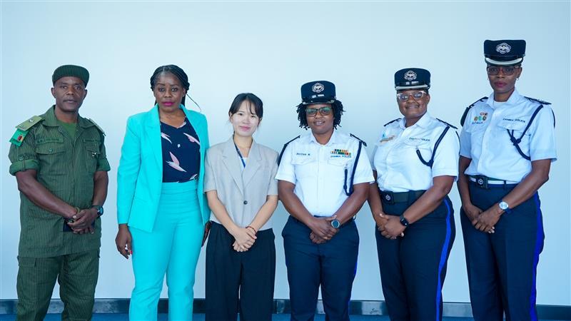 Six people in uniforms and business attire posing in a line against a light blue background