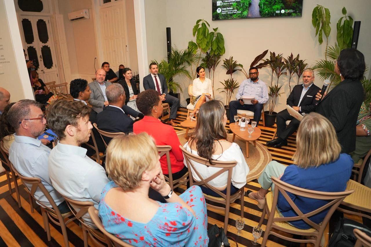 Photo: Group of people seated in a circle in a plant-filled room listening to a speaker.
