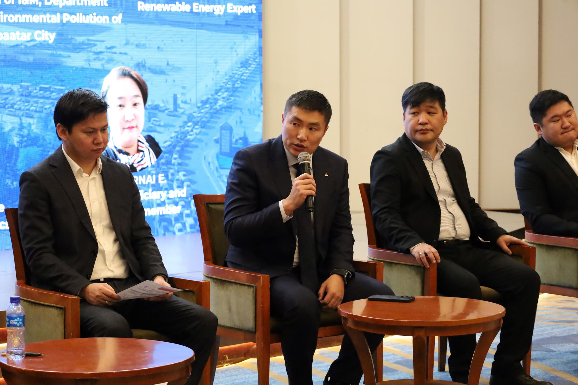 Panel of four men in suits on stage; center man speaks into microphone.