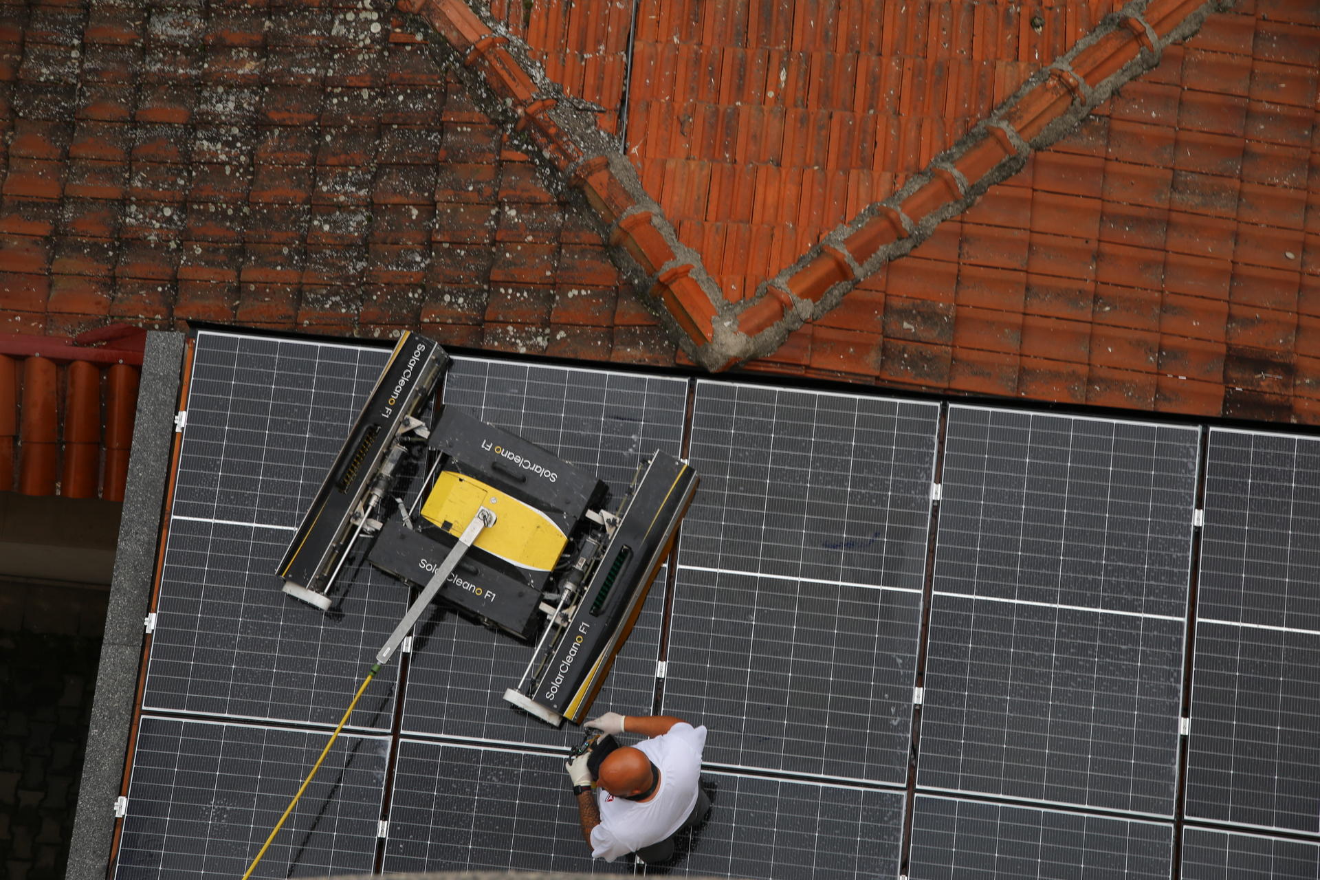 Worker in safety gear on a tiled roof installing solar panels.