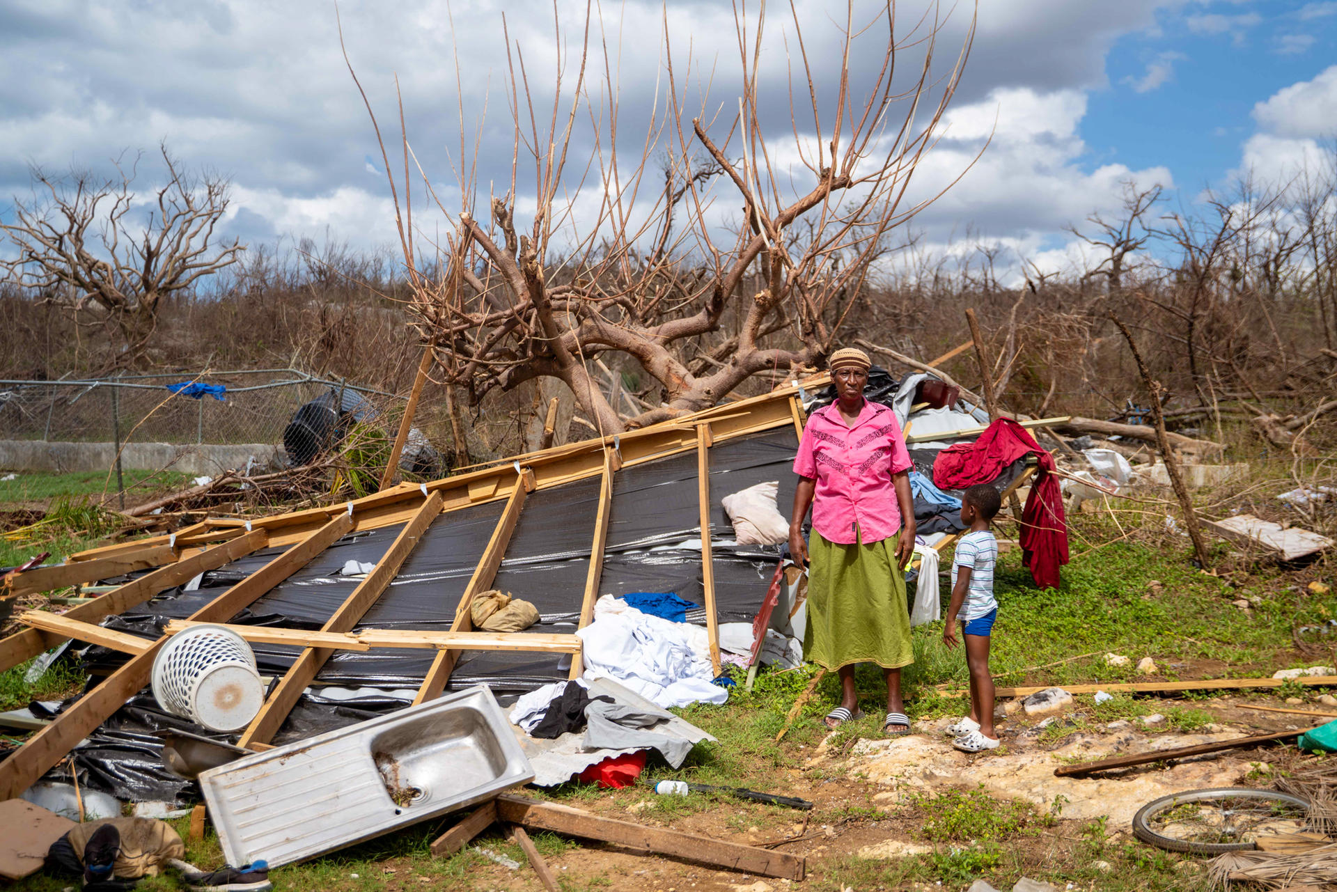 Two children in bright jackets explore wreckage and a toppled tree after a storm.