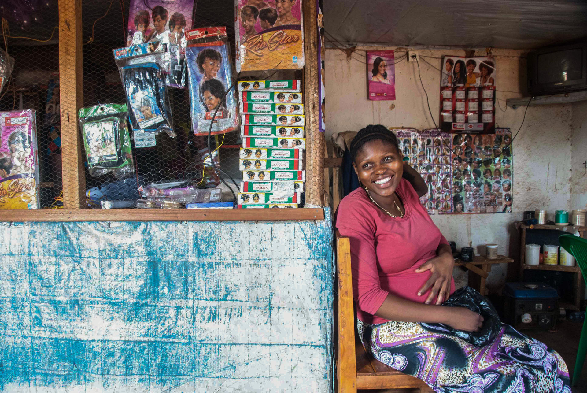 Photograph of a small shop interior with posters, blue counter, and a woman in pink seated inside.
