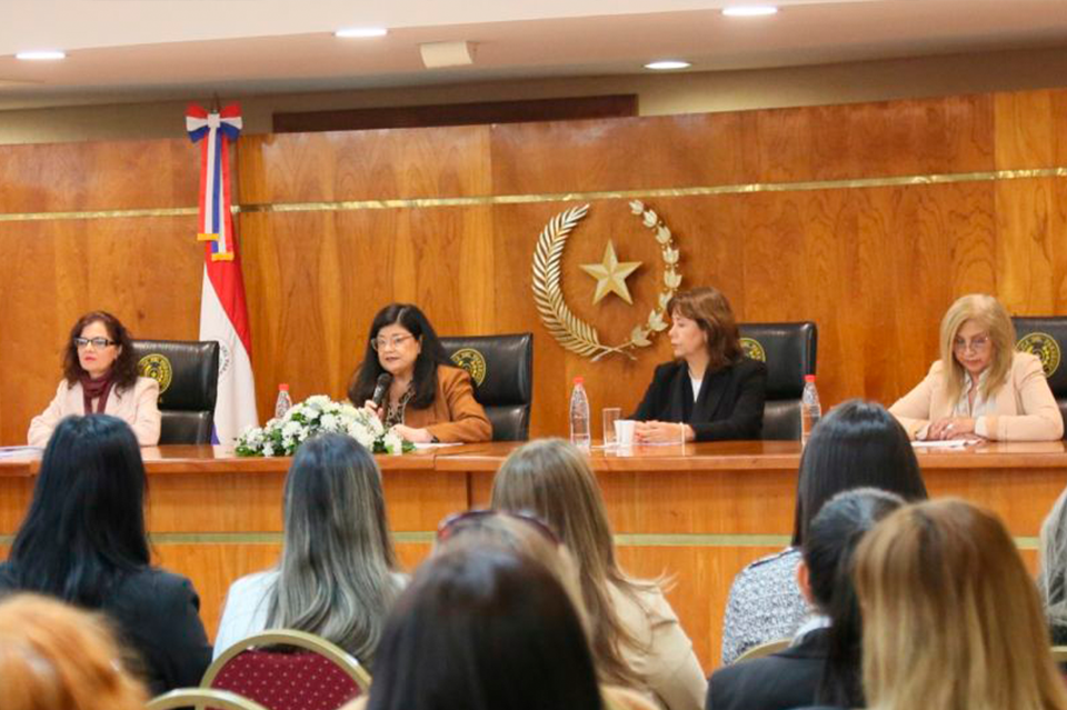 Officials seated at a long desk on a wood-paneled stage; Indonesian flag visible, audience.
