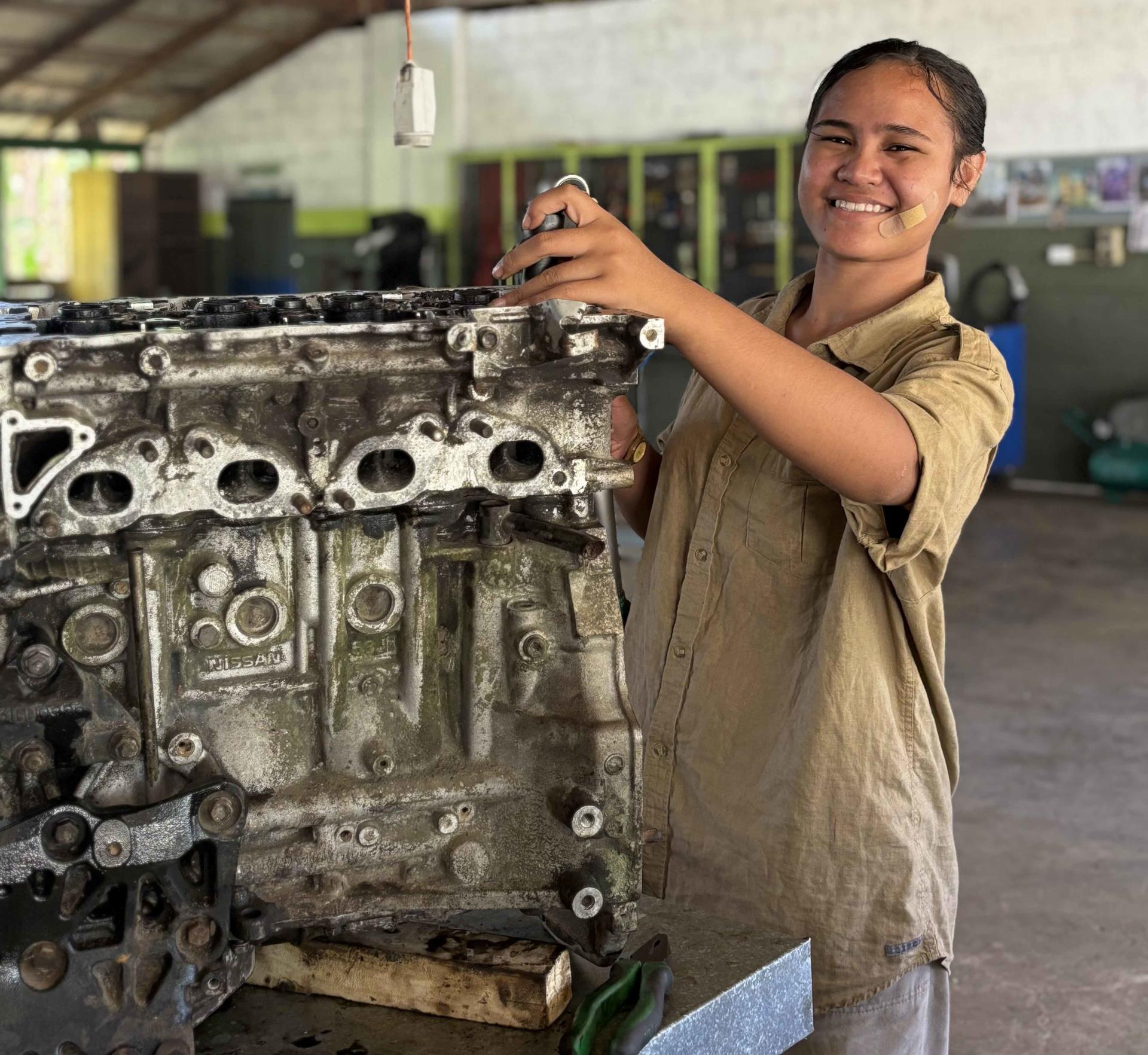 Person in a workshop examines a metal engine block on a stand.