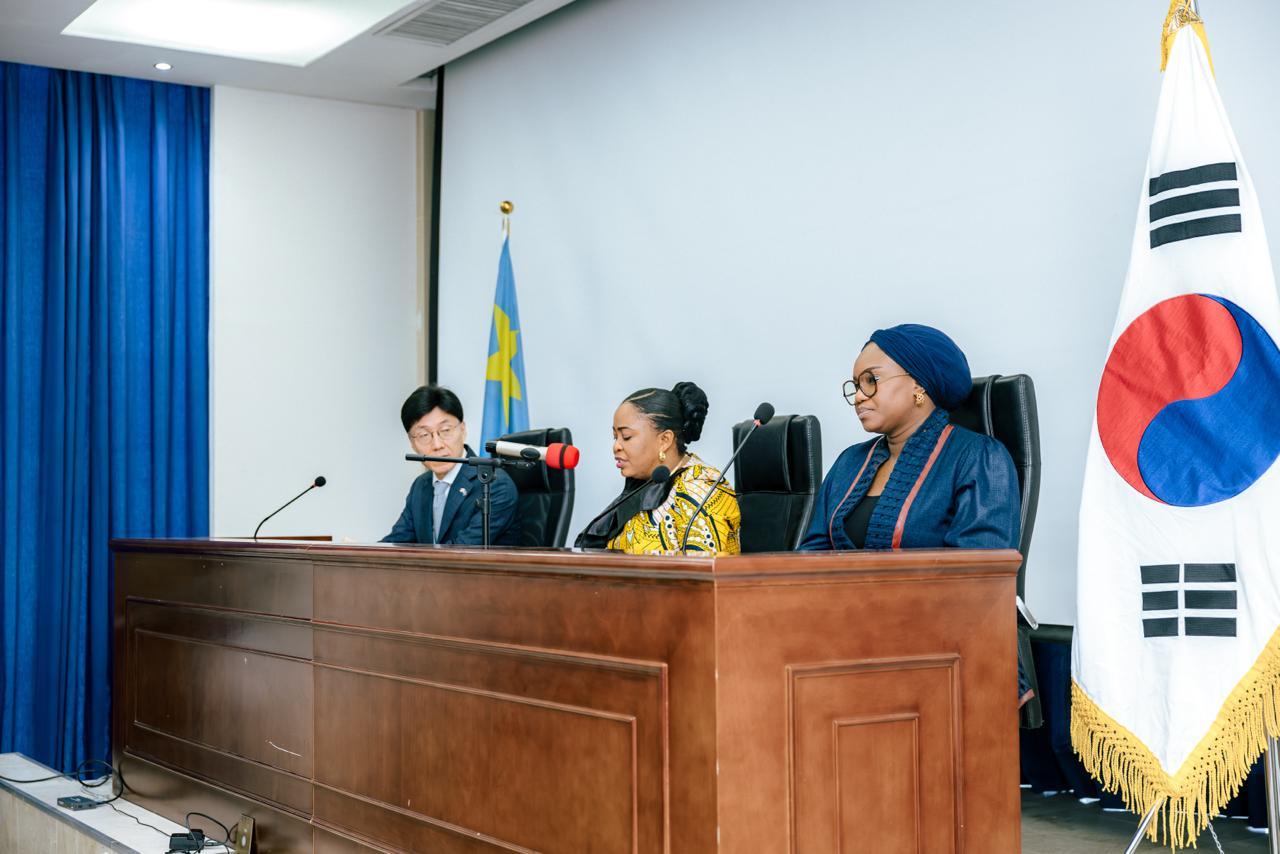 Four panelists at a wooden dais with microphones, blue curtain, and South Korean flag.