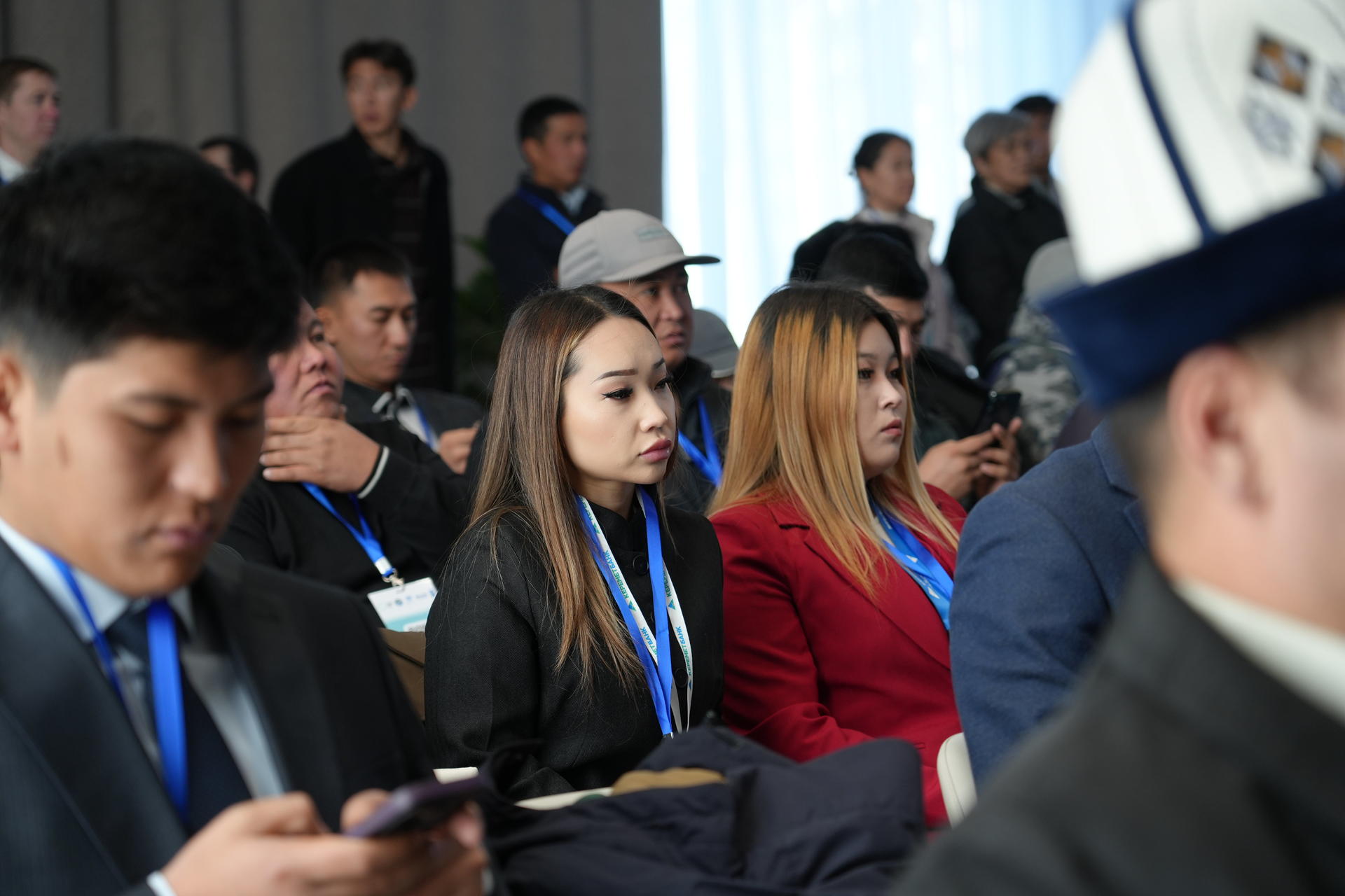 Audience at indoor ceremony; attendees wear medals on blue ribbons, seated facing forward.