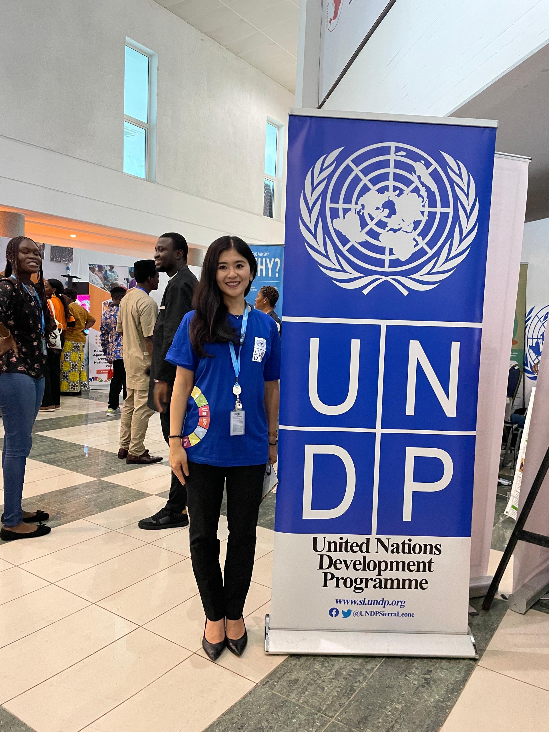 Two women stand near a UNDP banner in a busy indoor hall.