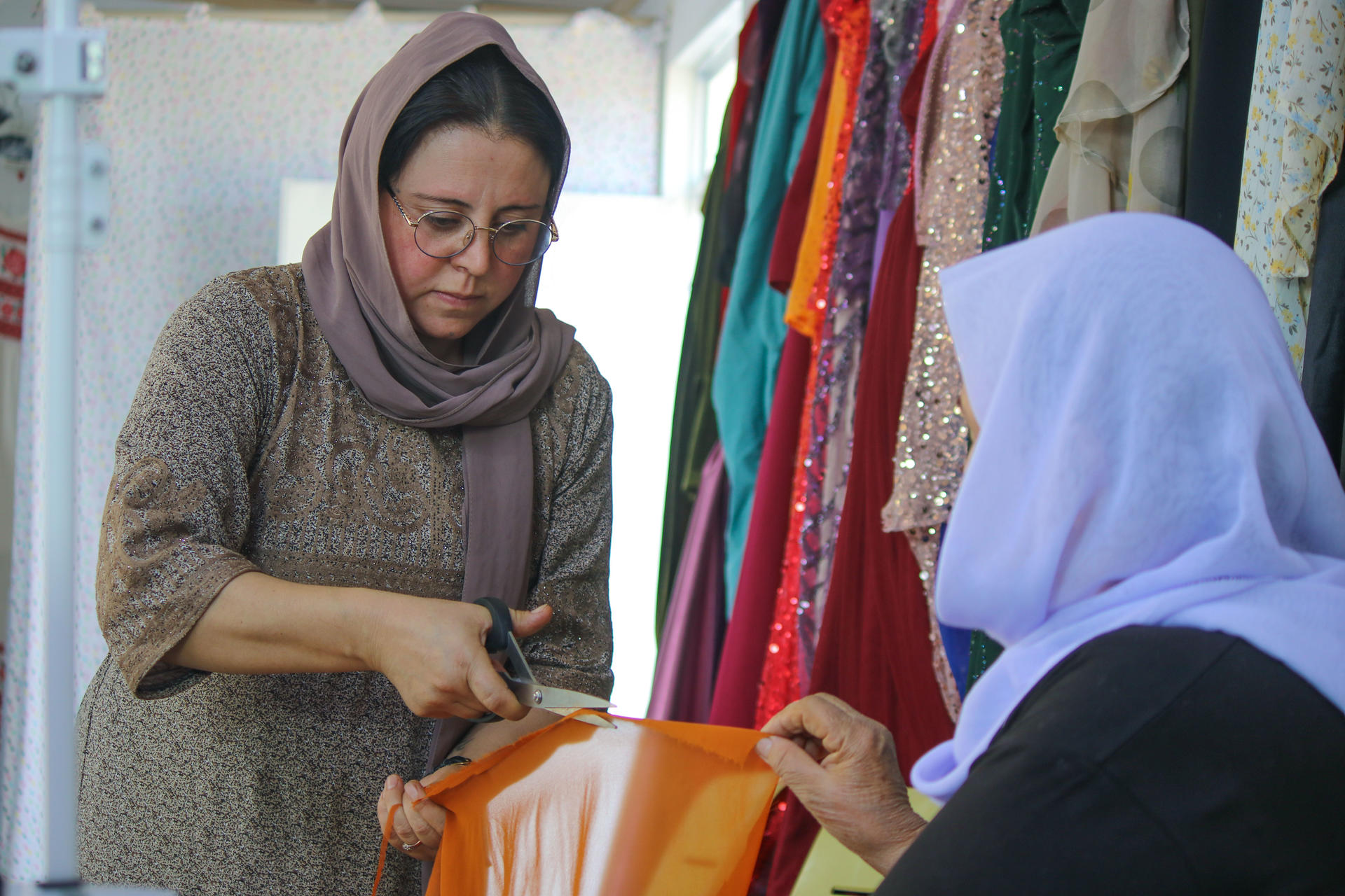Two hijab-wearing women inspect an orange handbag in a clothing shop.