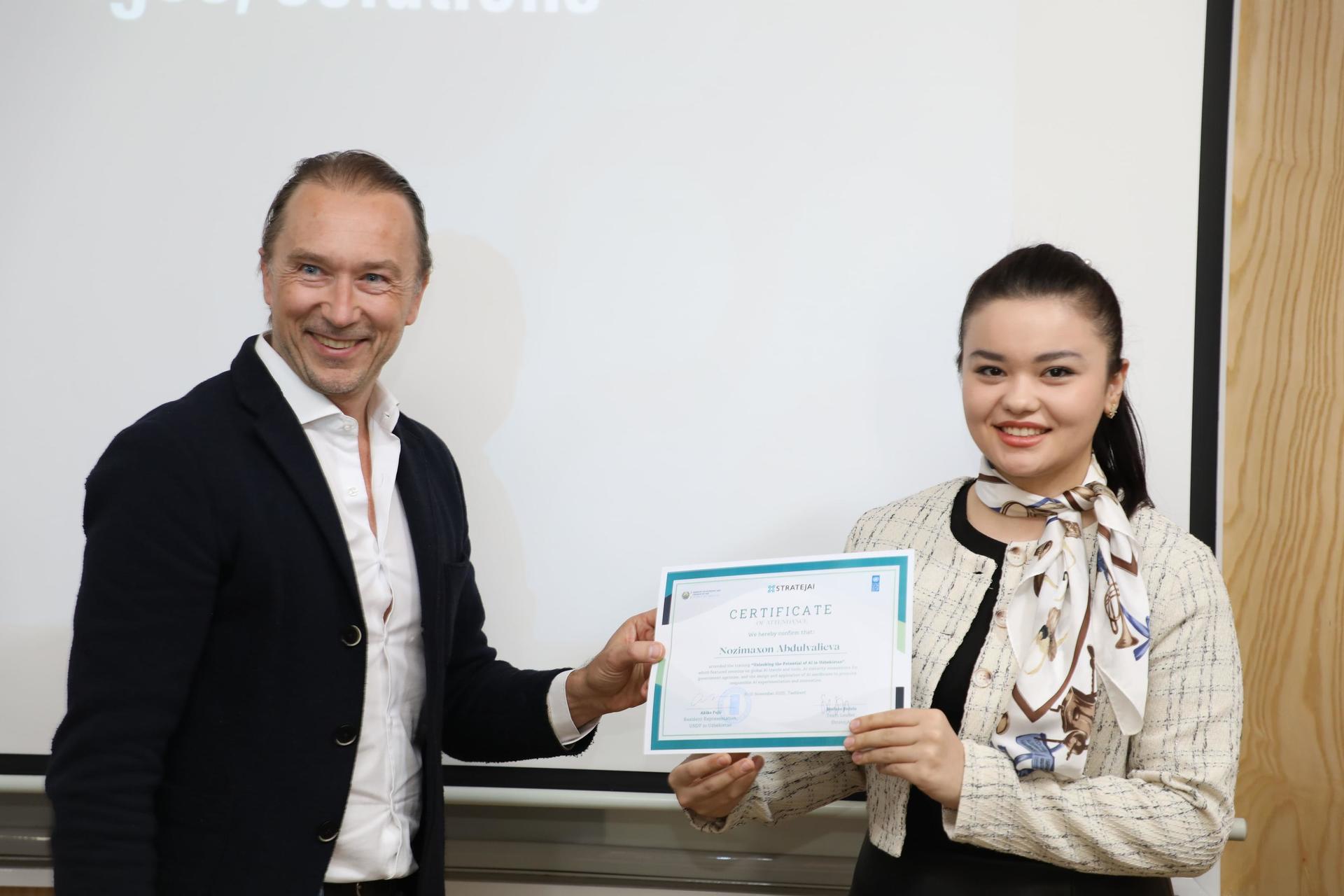 Two people in formal attire exchange a certificate in front of a projection screen.