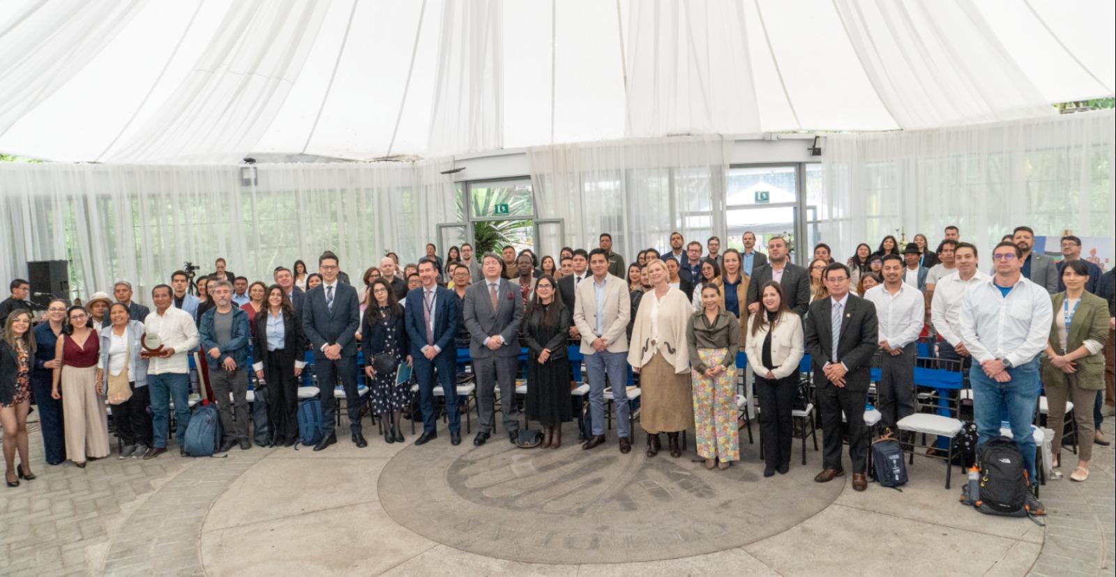 Group photo of diverse attendees in business attire inside a bright white tent.