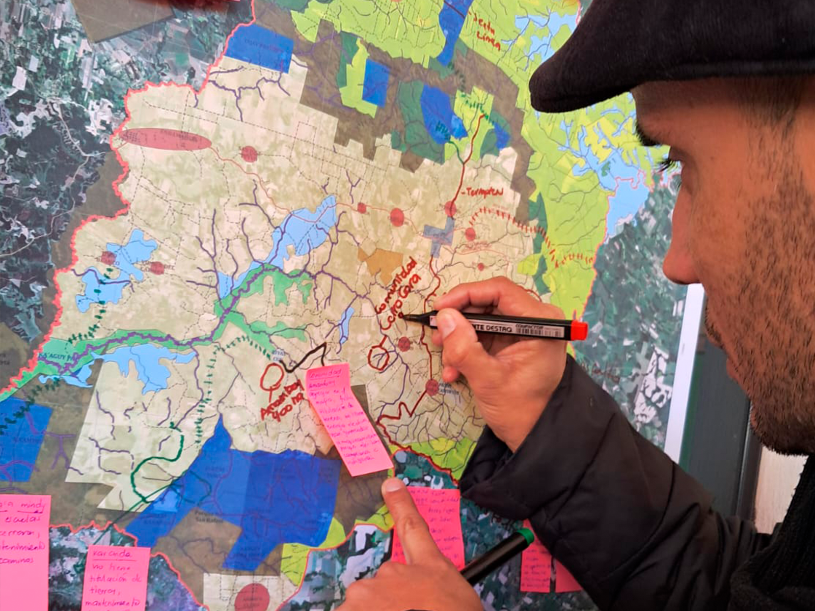 Hand writing on a large color-coded map covered with pink sticky notes.