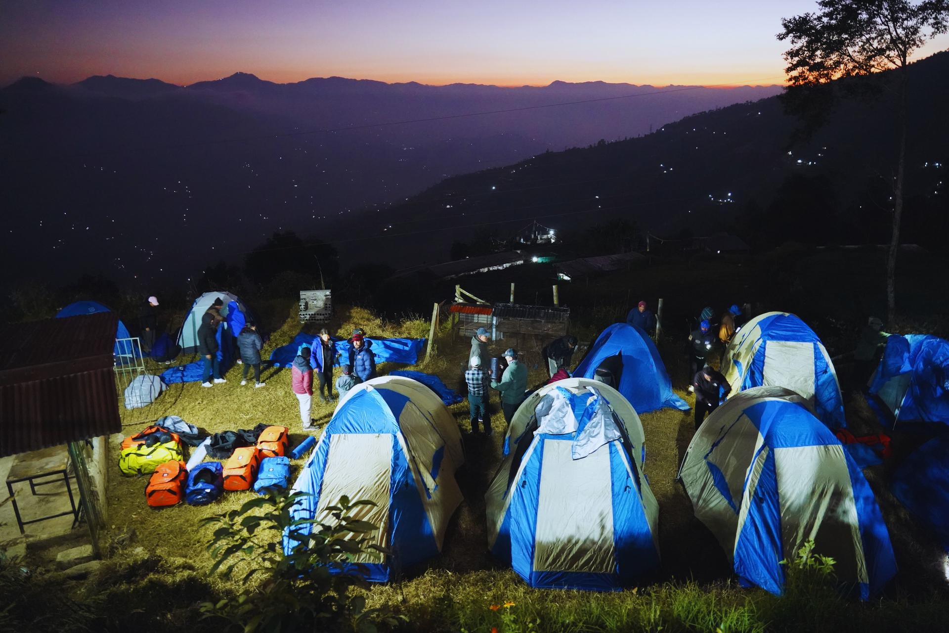Blue and white tents pitched on a grassy hillside at dusk, with distant mountains.