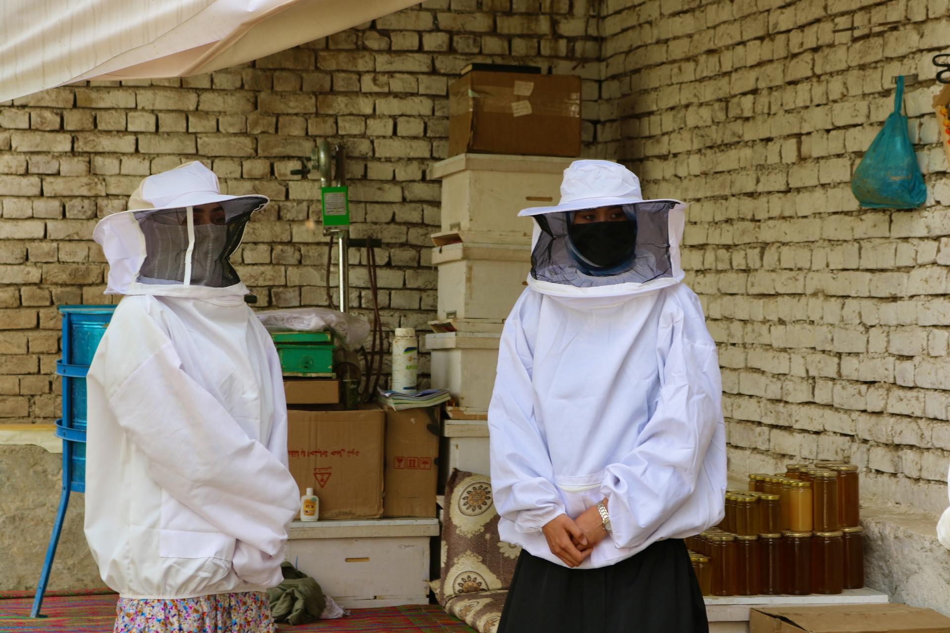 Photograph of two people in full PPE suits with veils, standing in a brick-walled room with boxes.