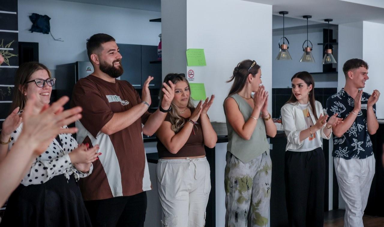 Diverse group standing in a row, clapping at an indoor event.