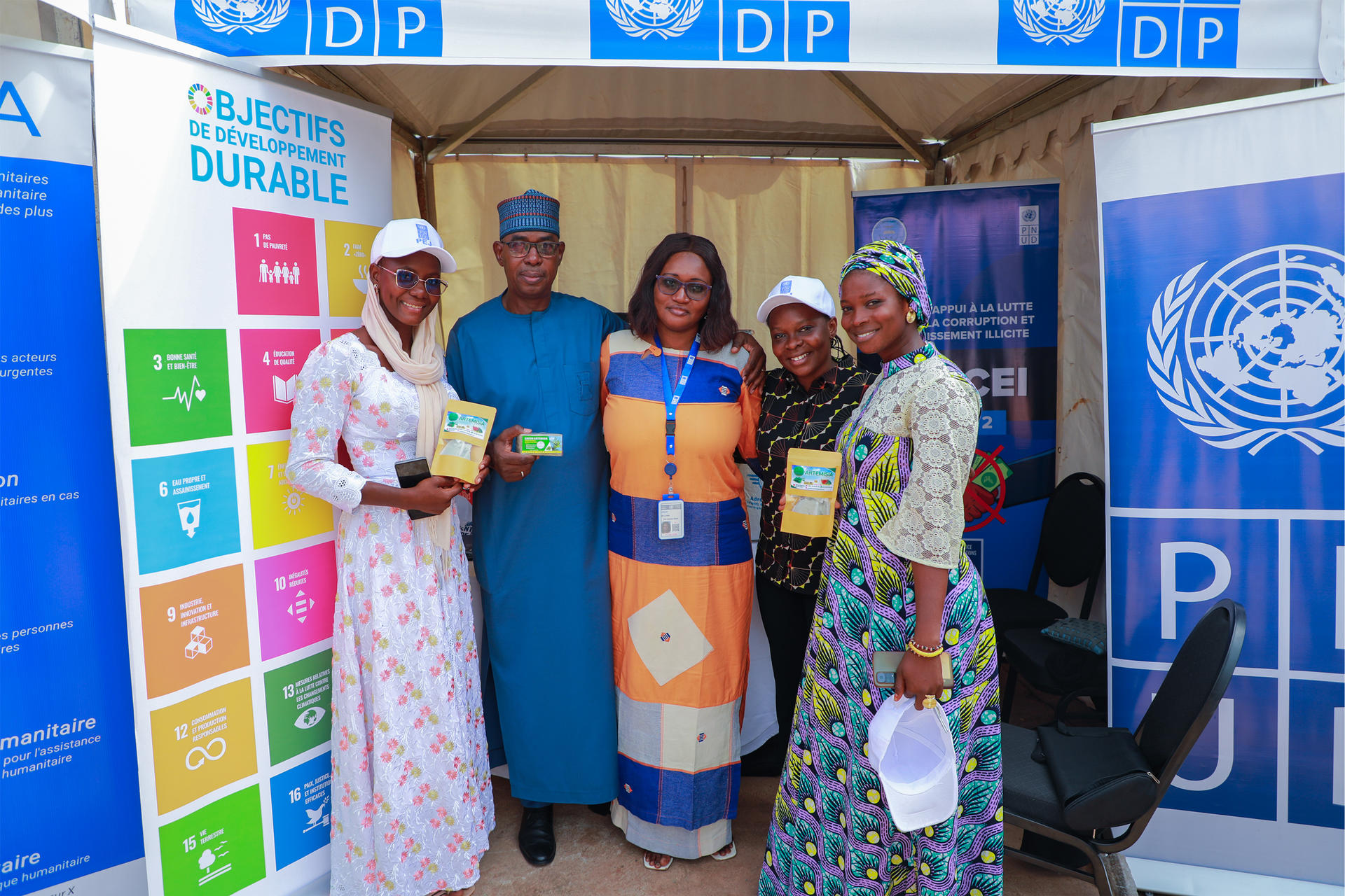 Five women in bright traditional dresses posing at a UNDP booth with SDG banners.