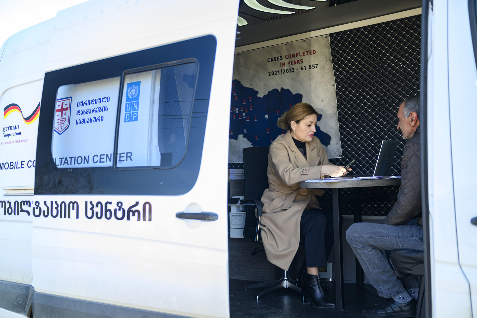 Photograph of two people inside a white and blue mobile service van with its side door open.