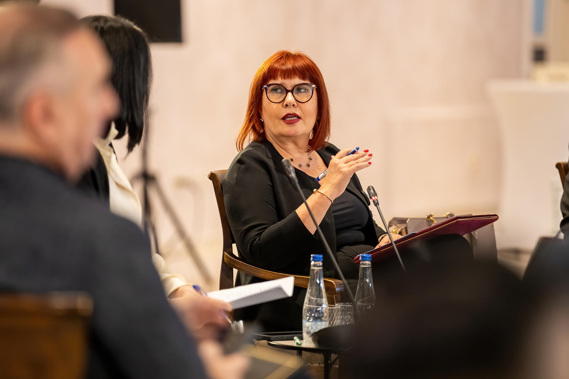 Photograph of a red-haired woman speaking into a microphone at a panel discussion.