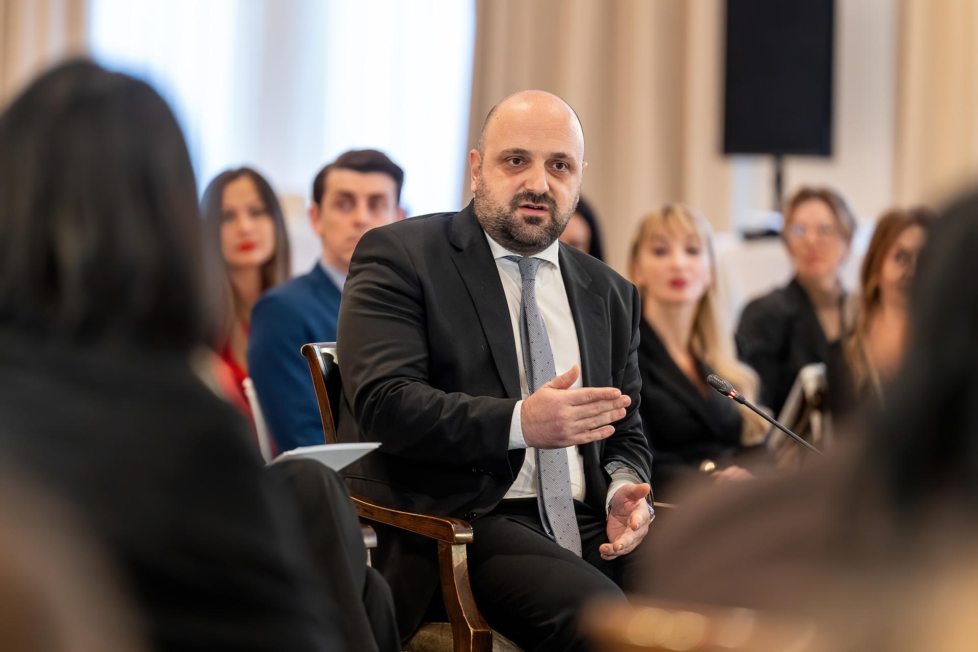 Photo: attendees at a formal meeting; central man in a suit holds a bottle.