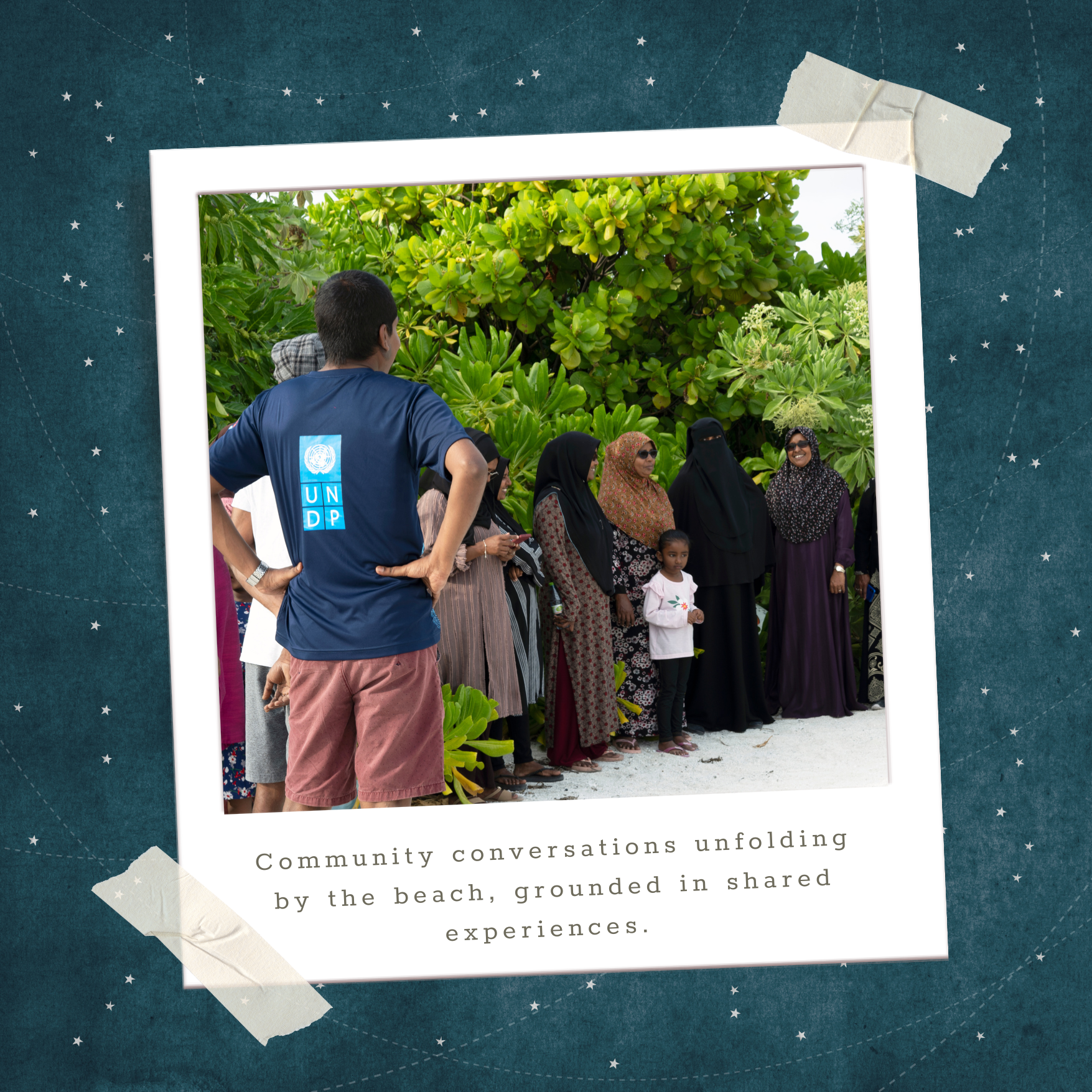 Photograph of a diverse group standing in a circle and talking outdoors among green trees.