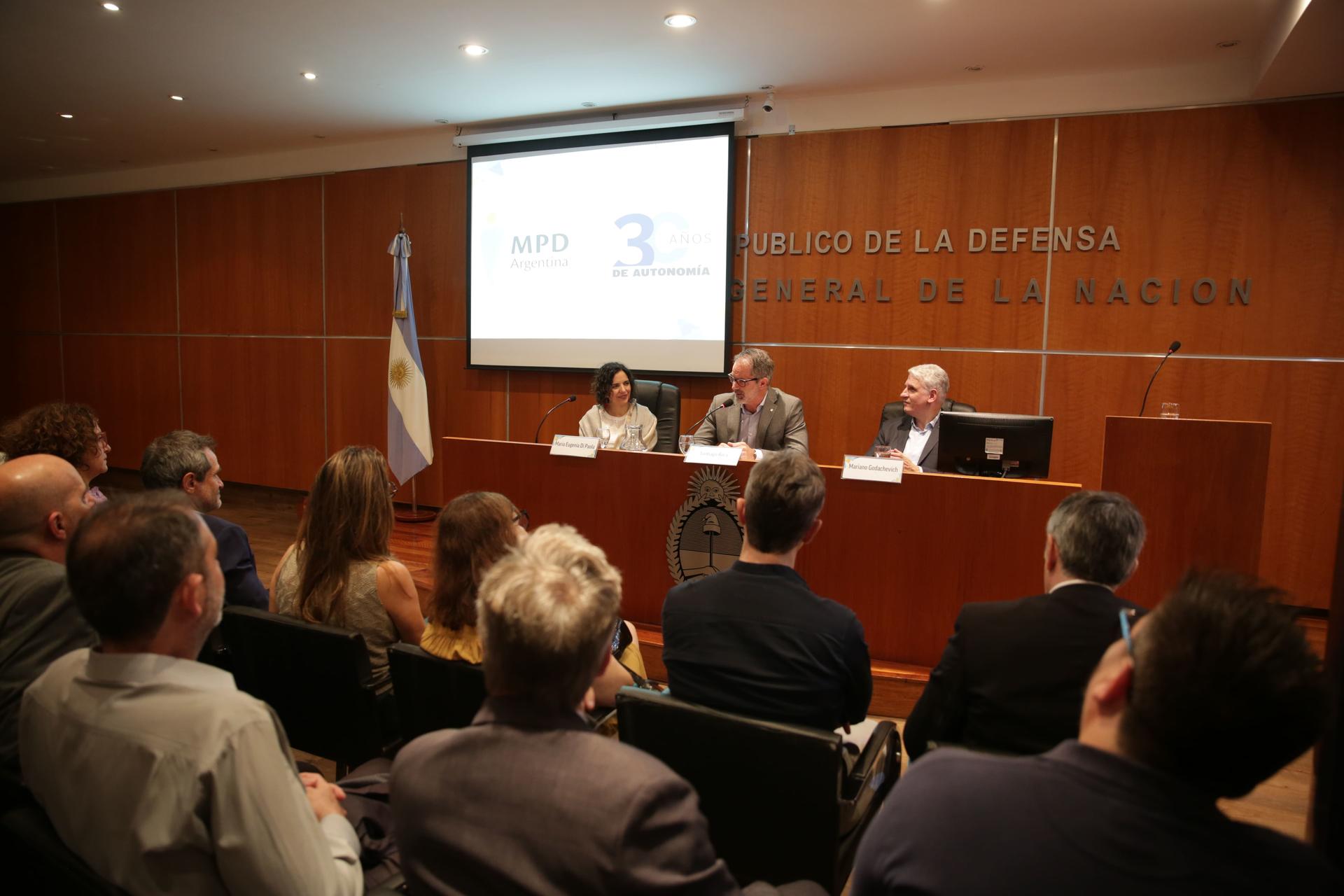 Photo of a panel discussion in a conference room, speaker at podium, audience seated.