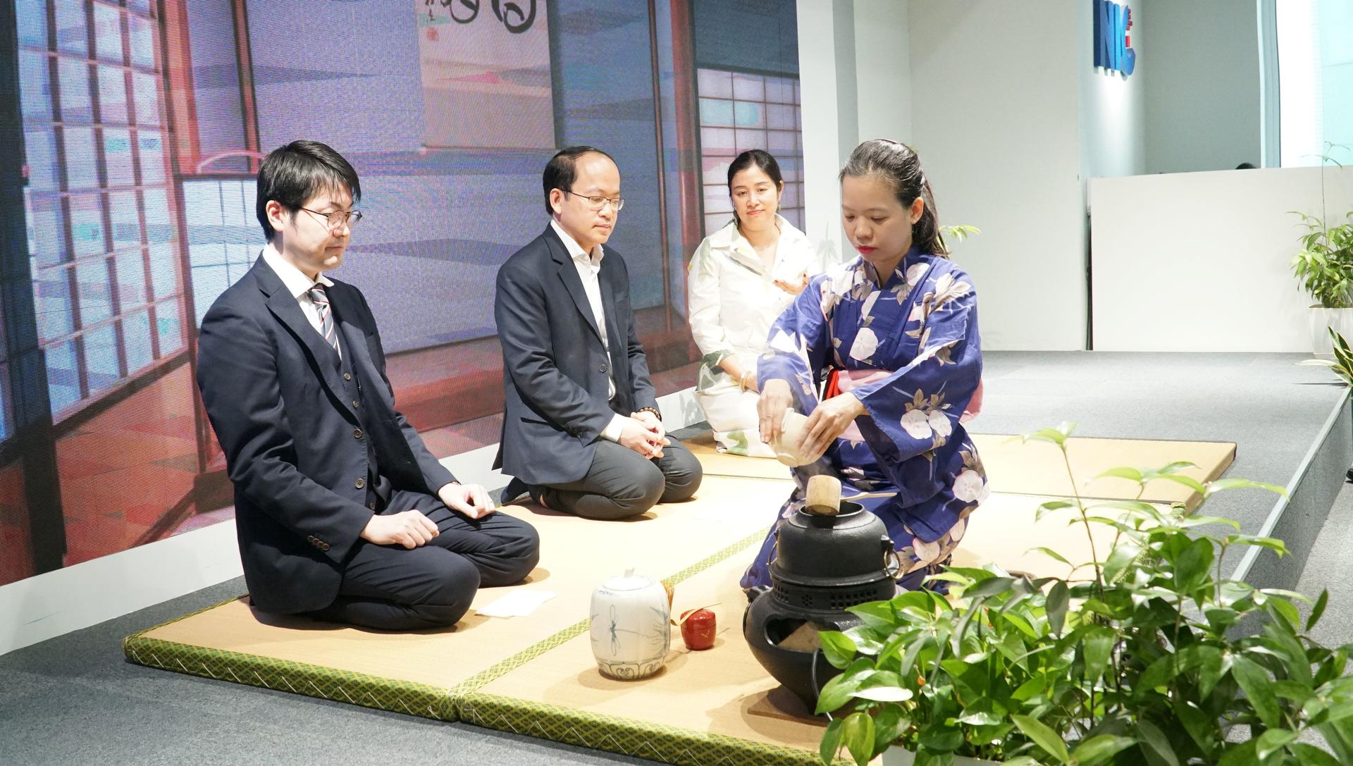 Five people kneel on tatami in a Japanese room; some in suits, others in traditional attire.