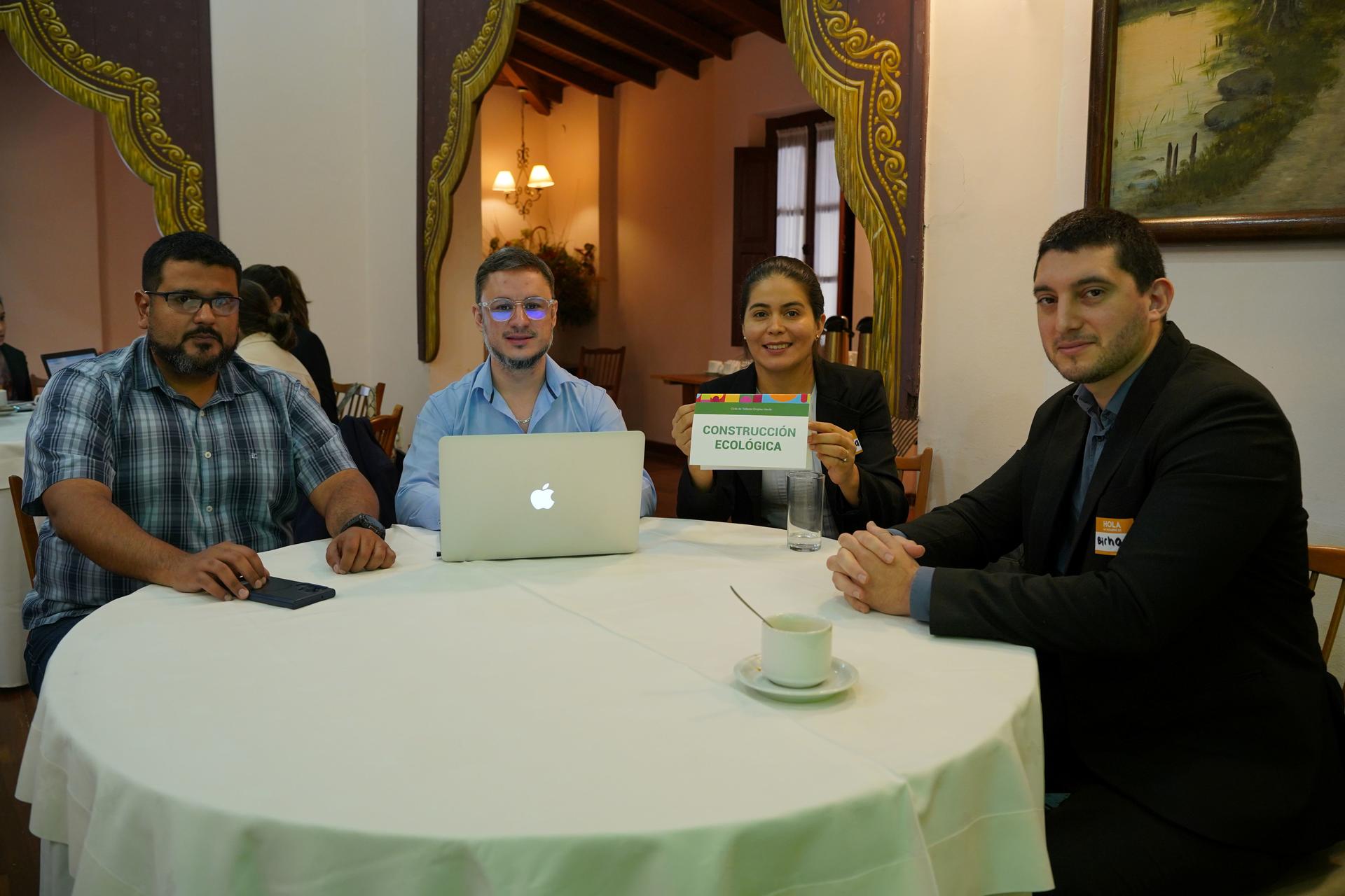 Group of people seated around a table in a cozy room; a laptop is open at the center.
