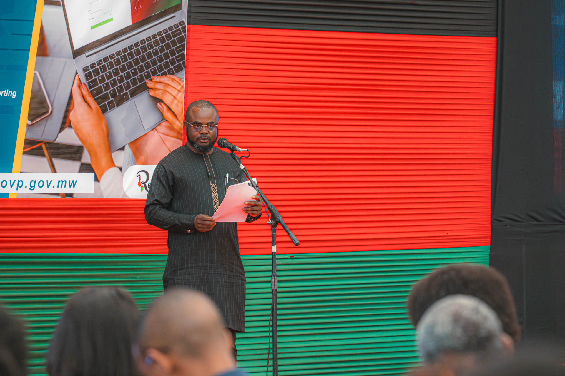 Photograph of a man on a stage speaking to an audience with a colorful LED backdrop.