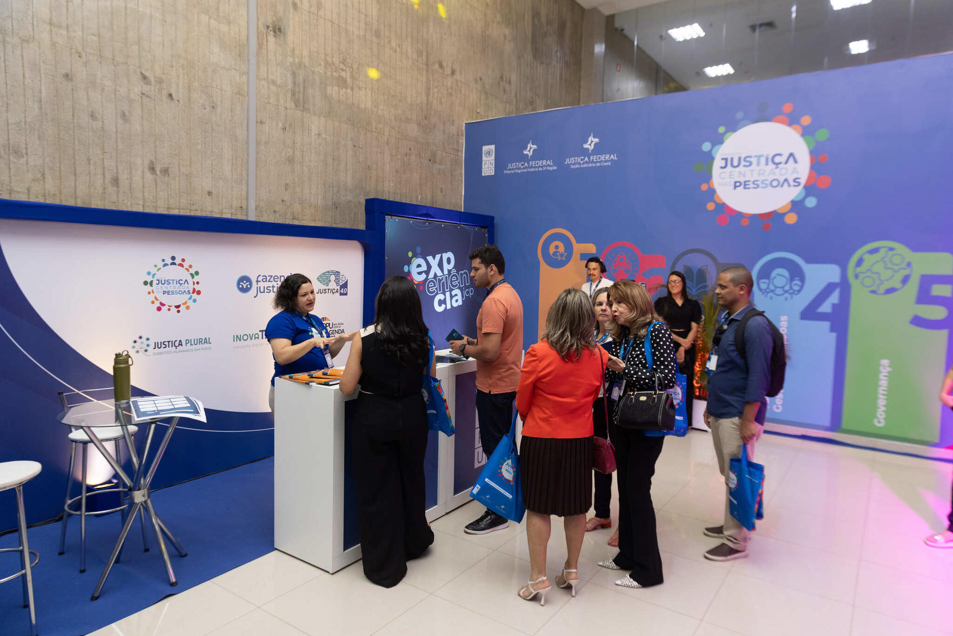 Photograph of a blue expo booth with attendees waiting at a counter.