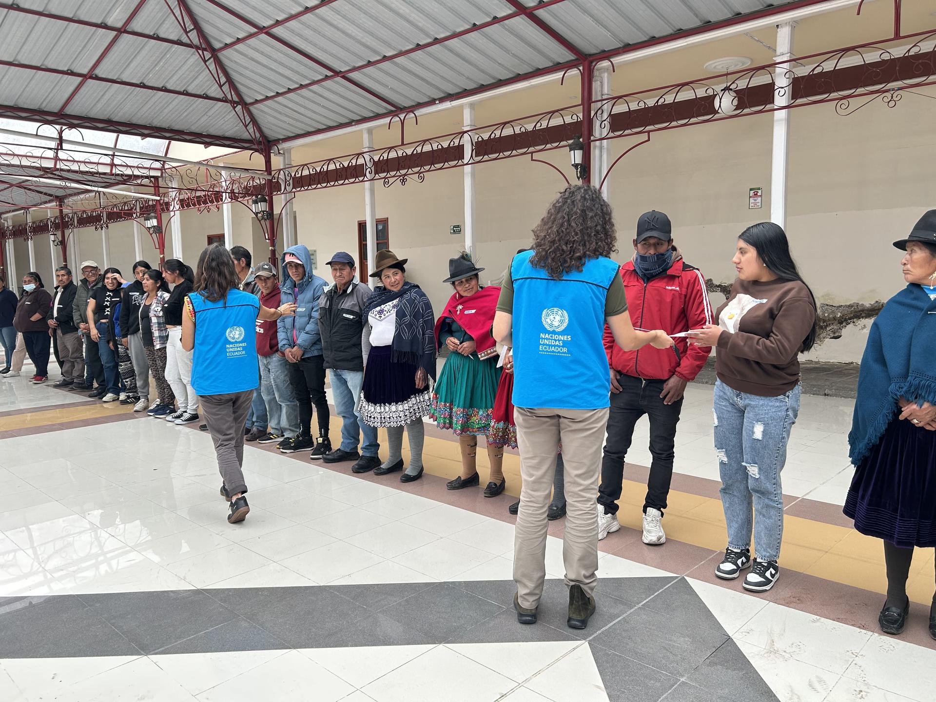 Group of people standing in a line under a covered walkway, some wearing blue shirts.