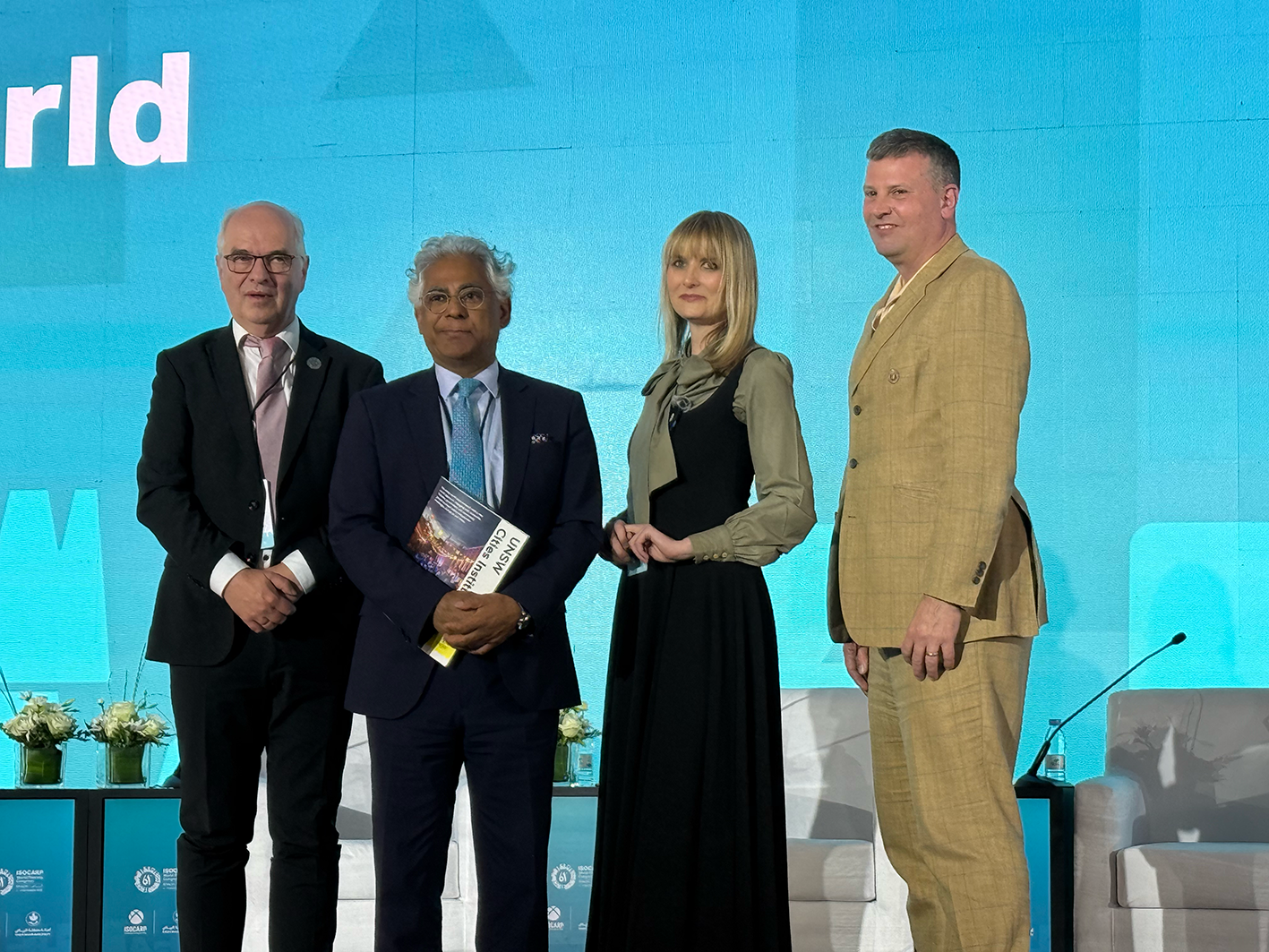 Photograph of four people on a stage at an awards ceremony against a blue backdrop.