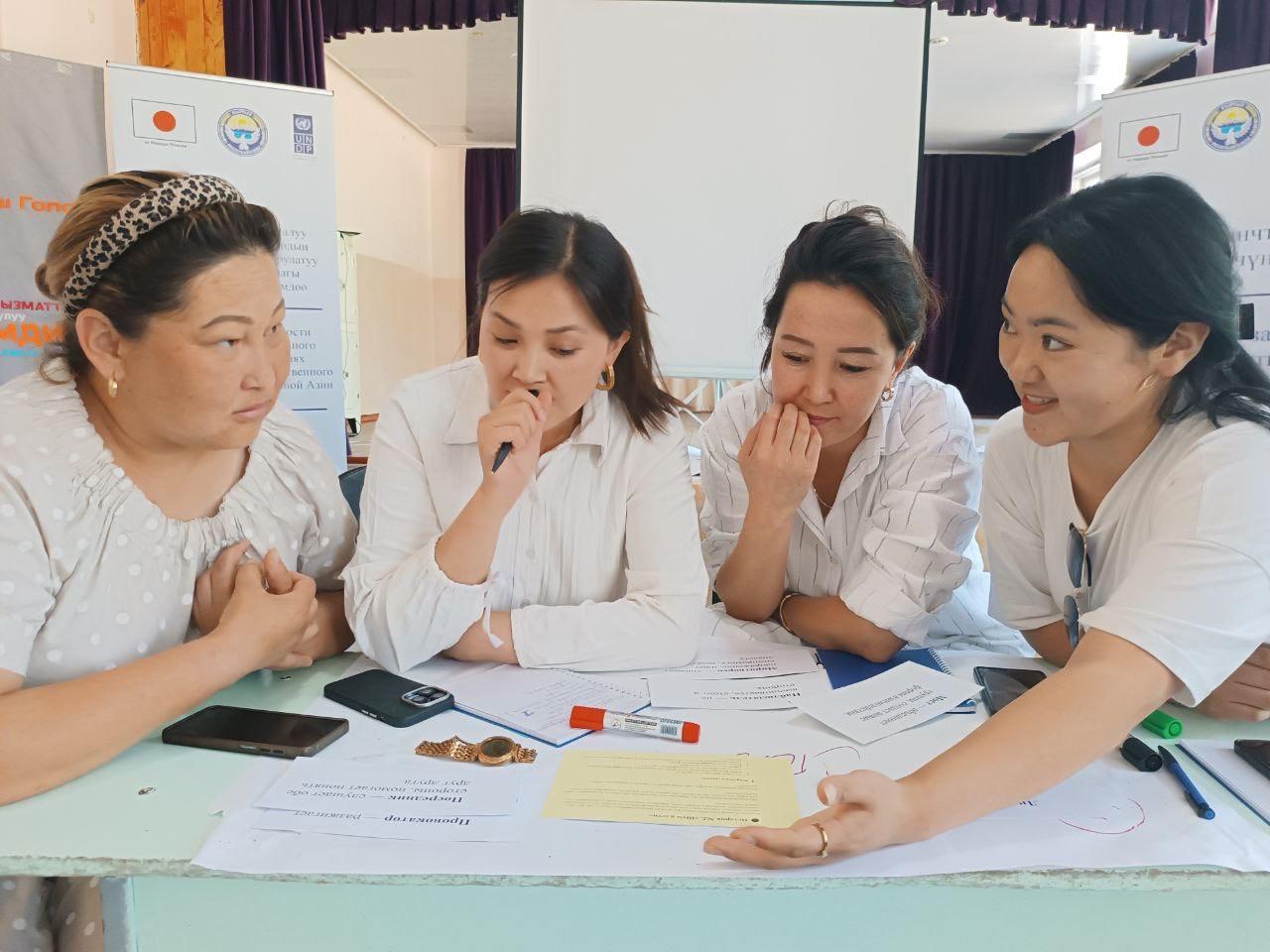Four people in white shirts sit at a light blue table with papers and a phone at a booth.