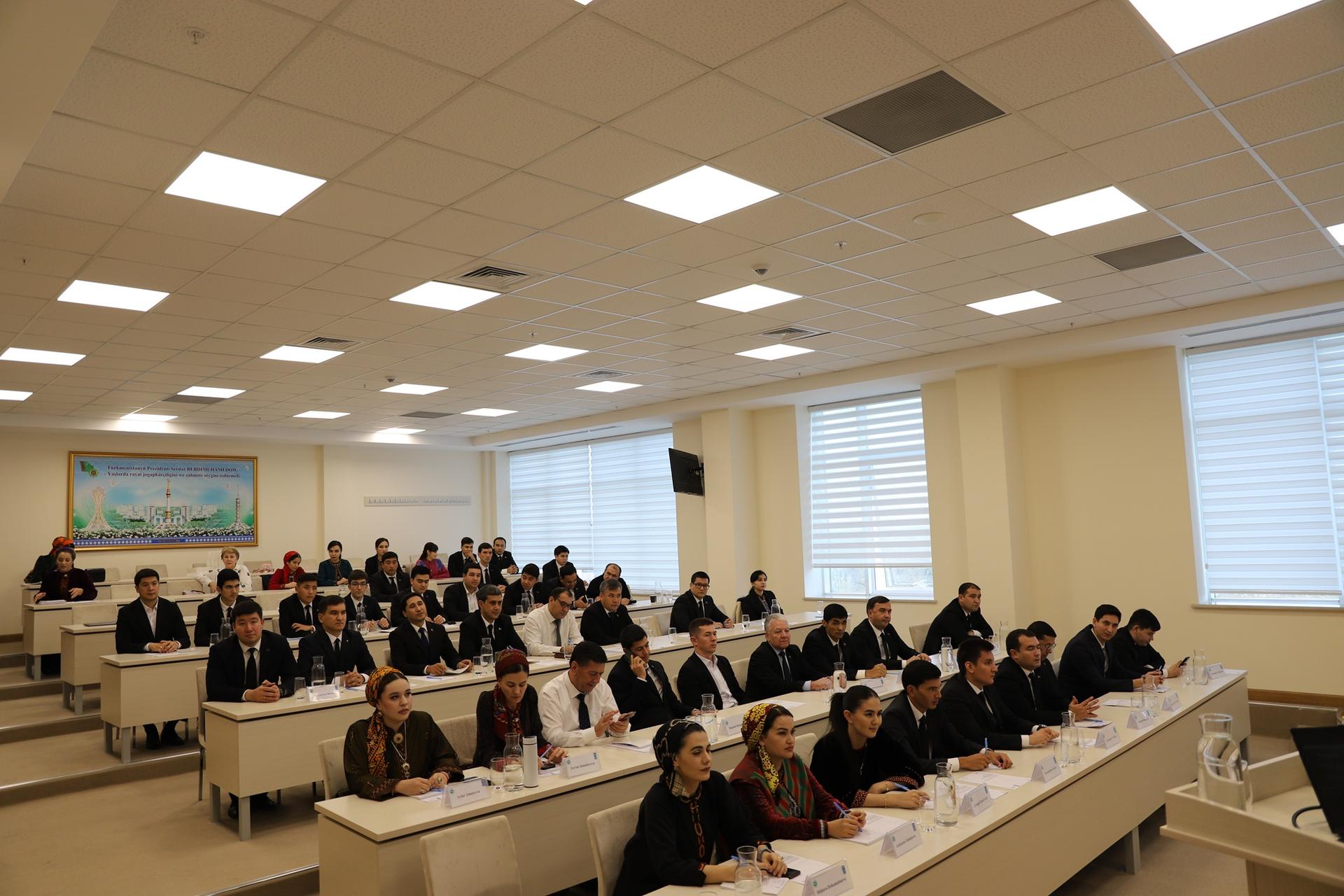 Large lecture hall full of students facing front as a lecturer speaks.