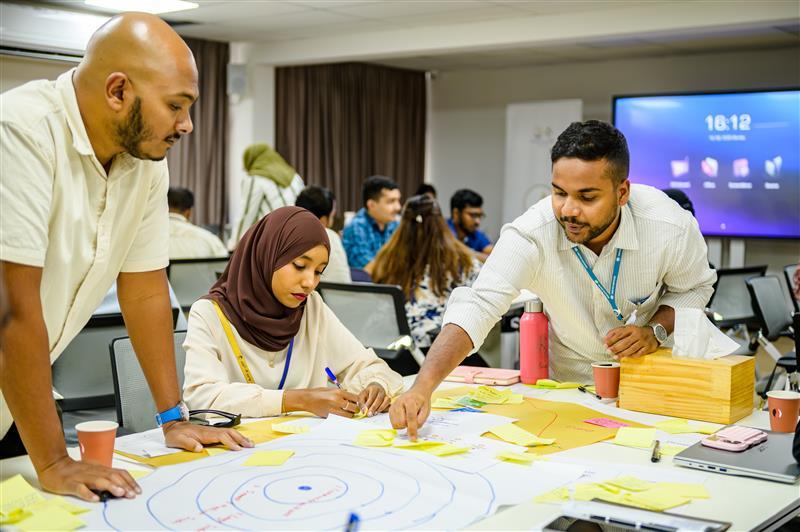 Group of people around a table working on a large colorful circular mural.