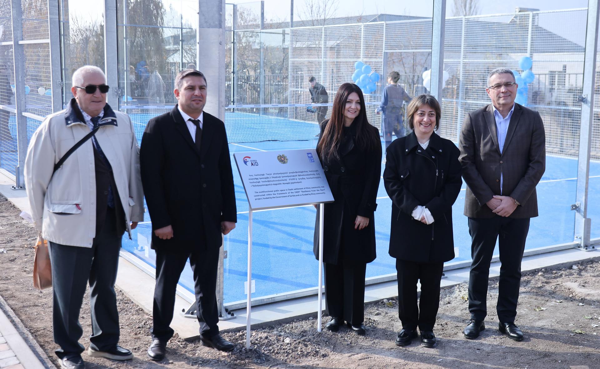 Photograph of six people in business attire standing along a harbor railing, with a sign at center.