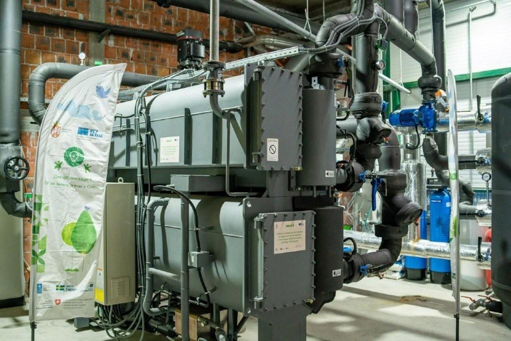 Industrial mechanical room with large black vertical equipment, piping and valves; banner on left.