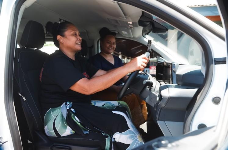 Photograph of two men in a car; driver holds steering wheel, passenger beside him smiling.