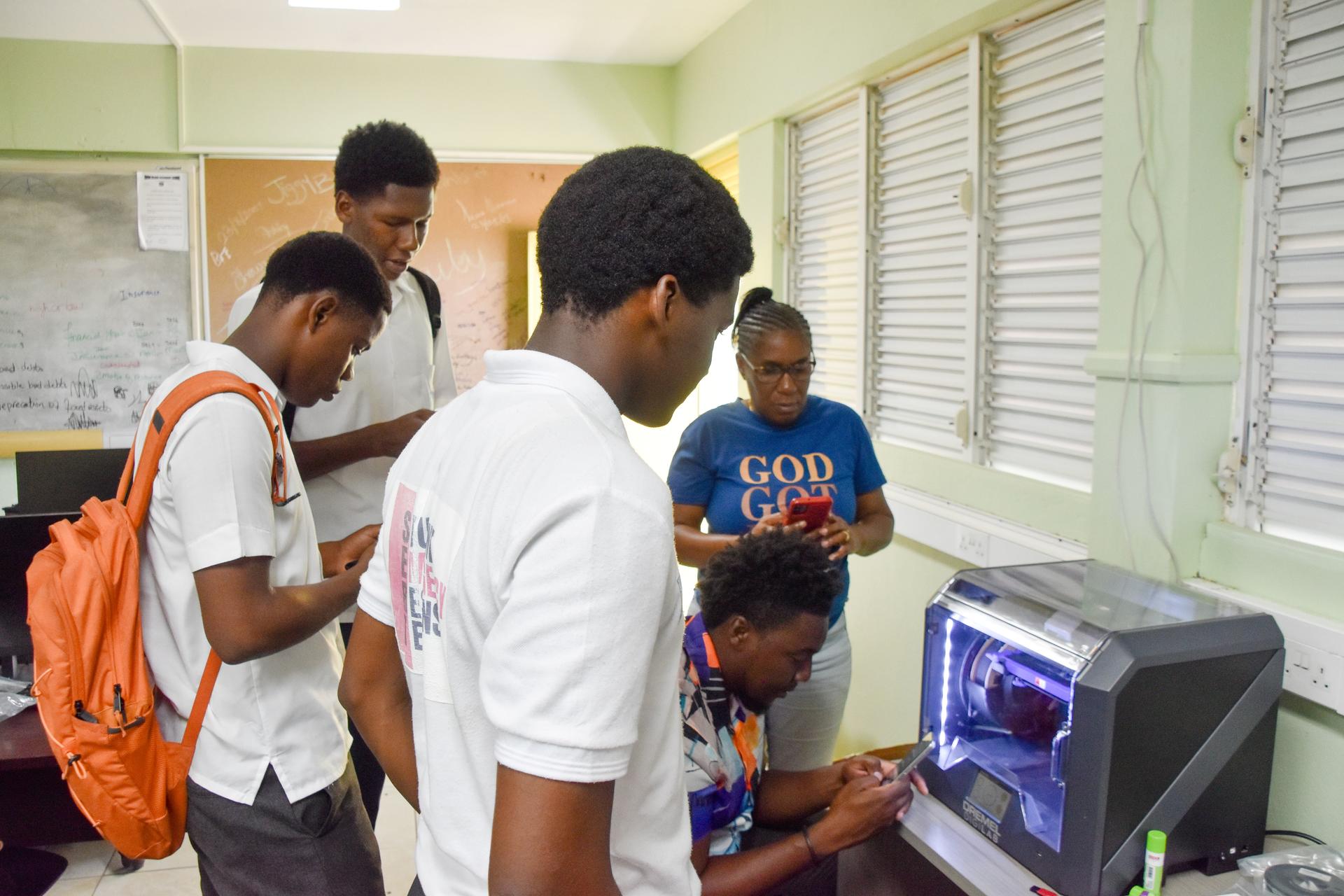 Group of students gathered around a computer in a bright classroom.
