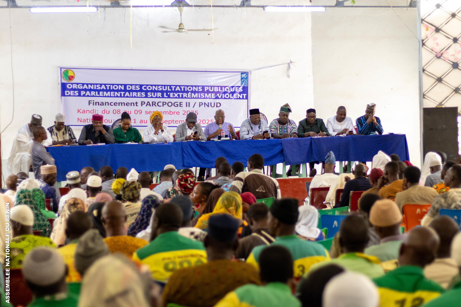 Photo: conference panel behind a long blue table onstage, banner in back, audience.