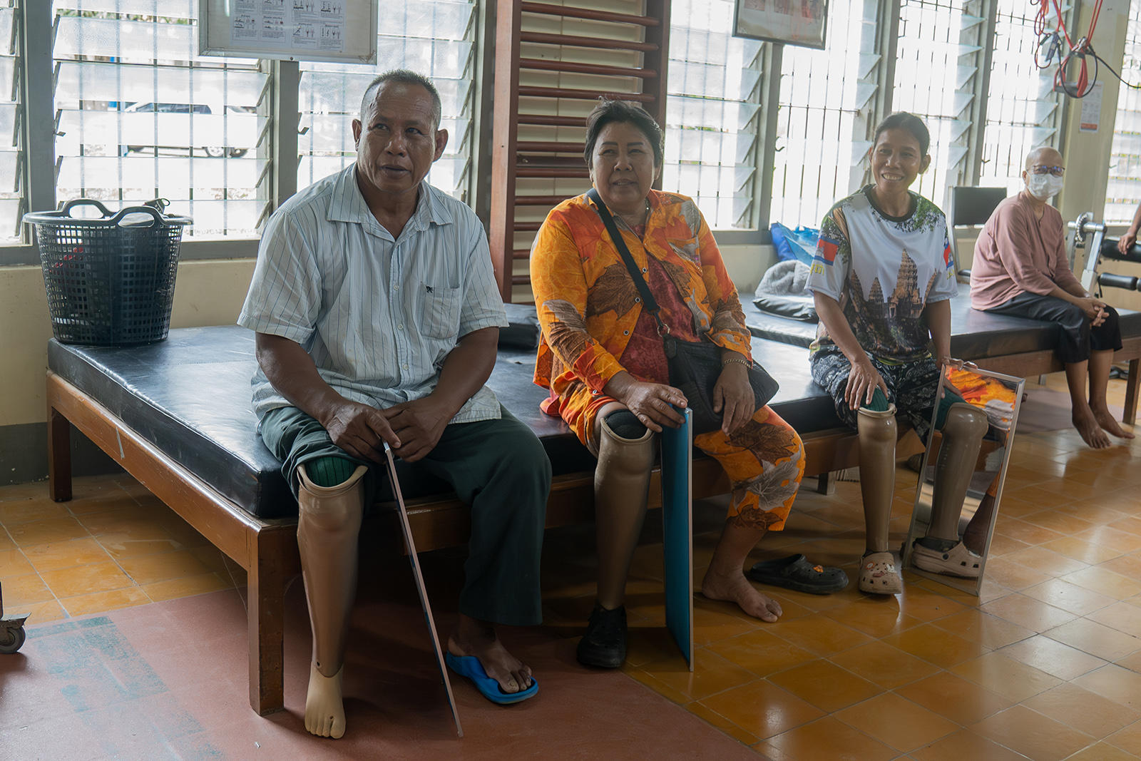 Group of people with prosthetic legs seated on benches in a bright waiting area.