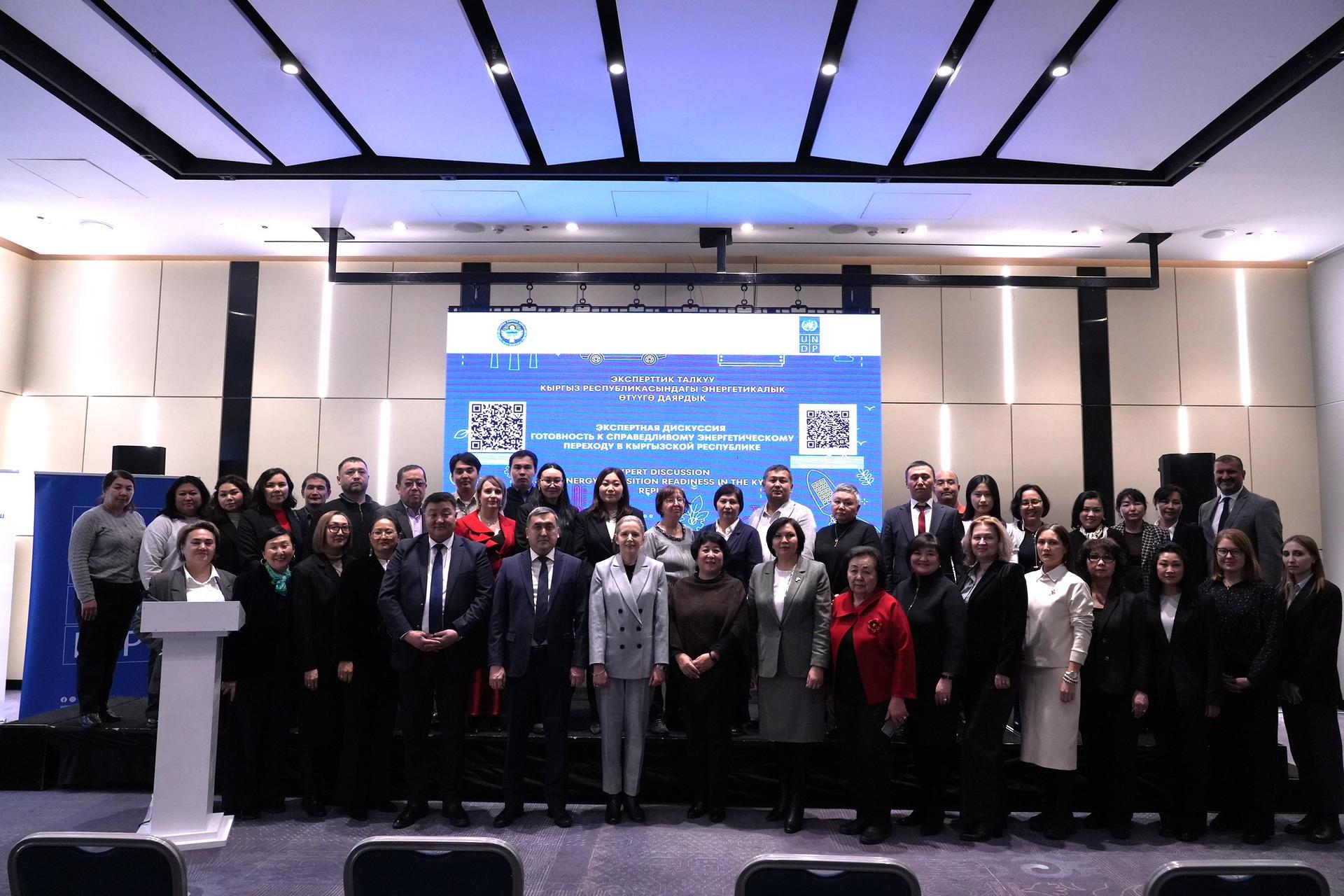 Group photo of a large conference crowd on stage with a blue banner backdrop.