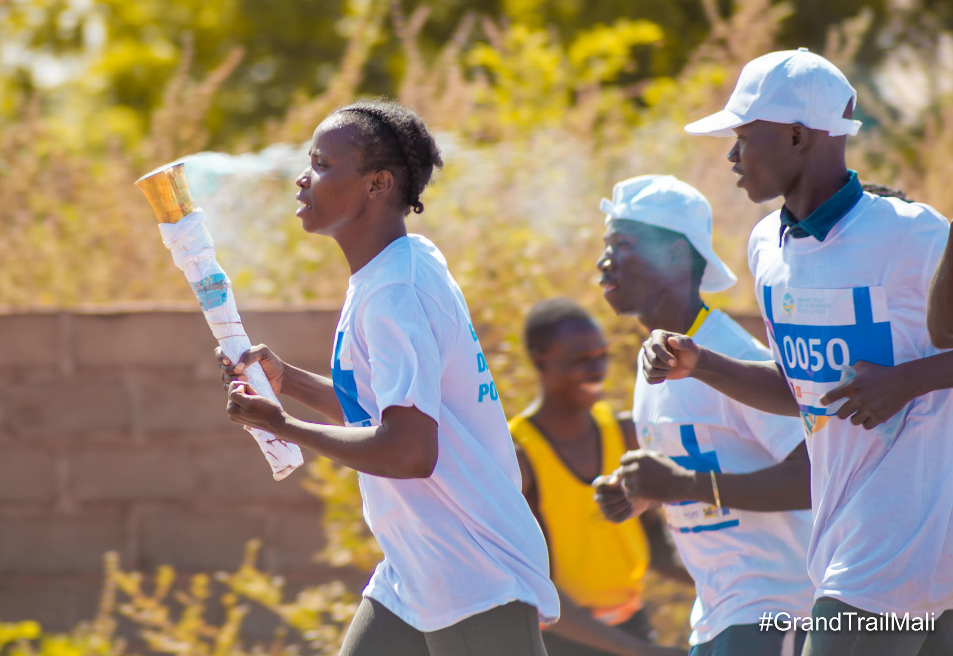Photograph of three runners in a sunny outdoor race; front runner reads a map.