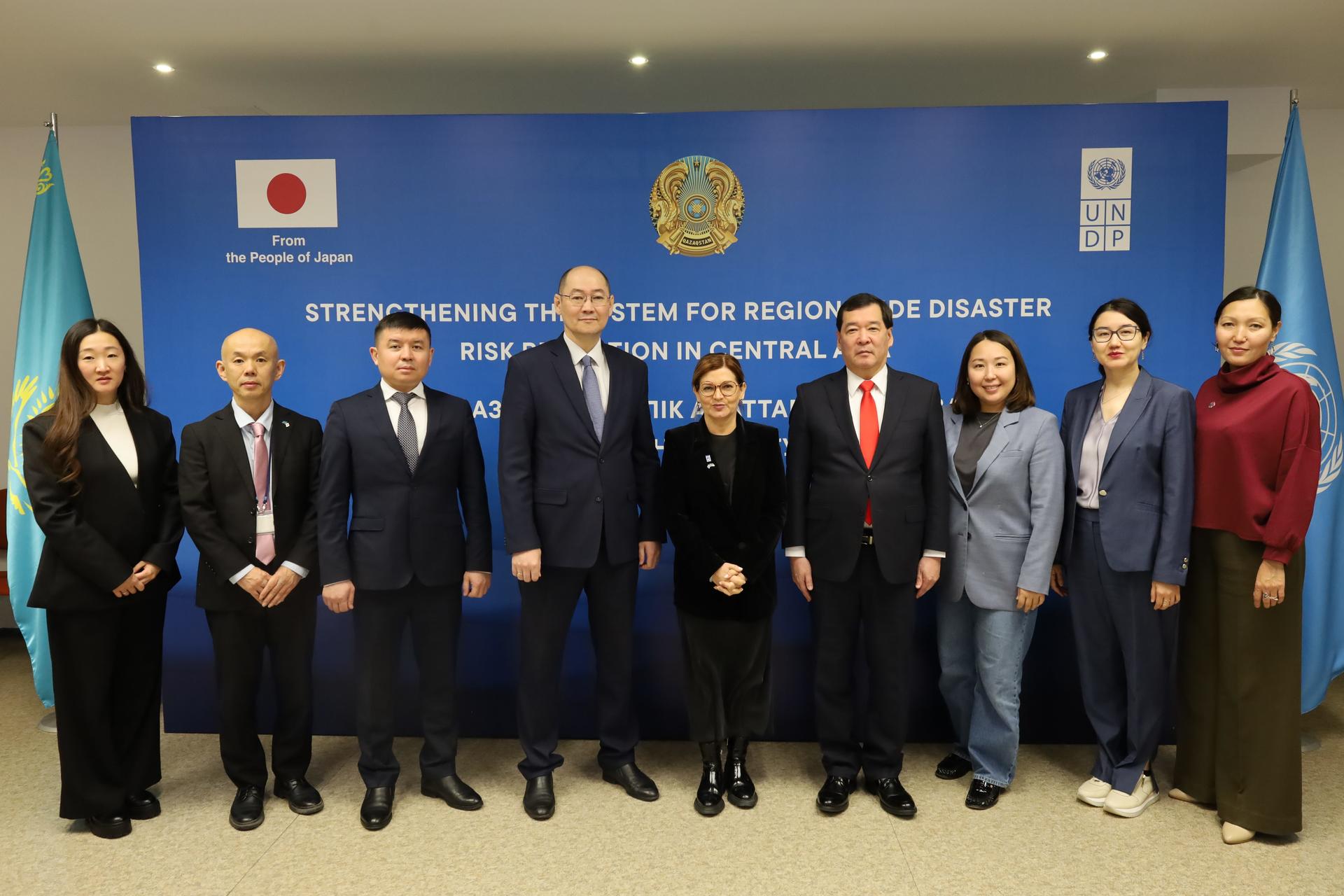 Officials in formal attire posing in a conference room with a blue banner and flags.