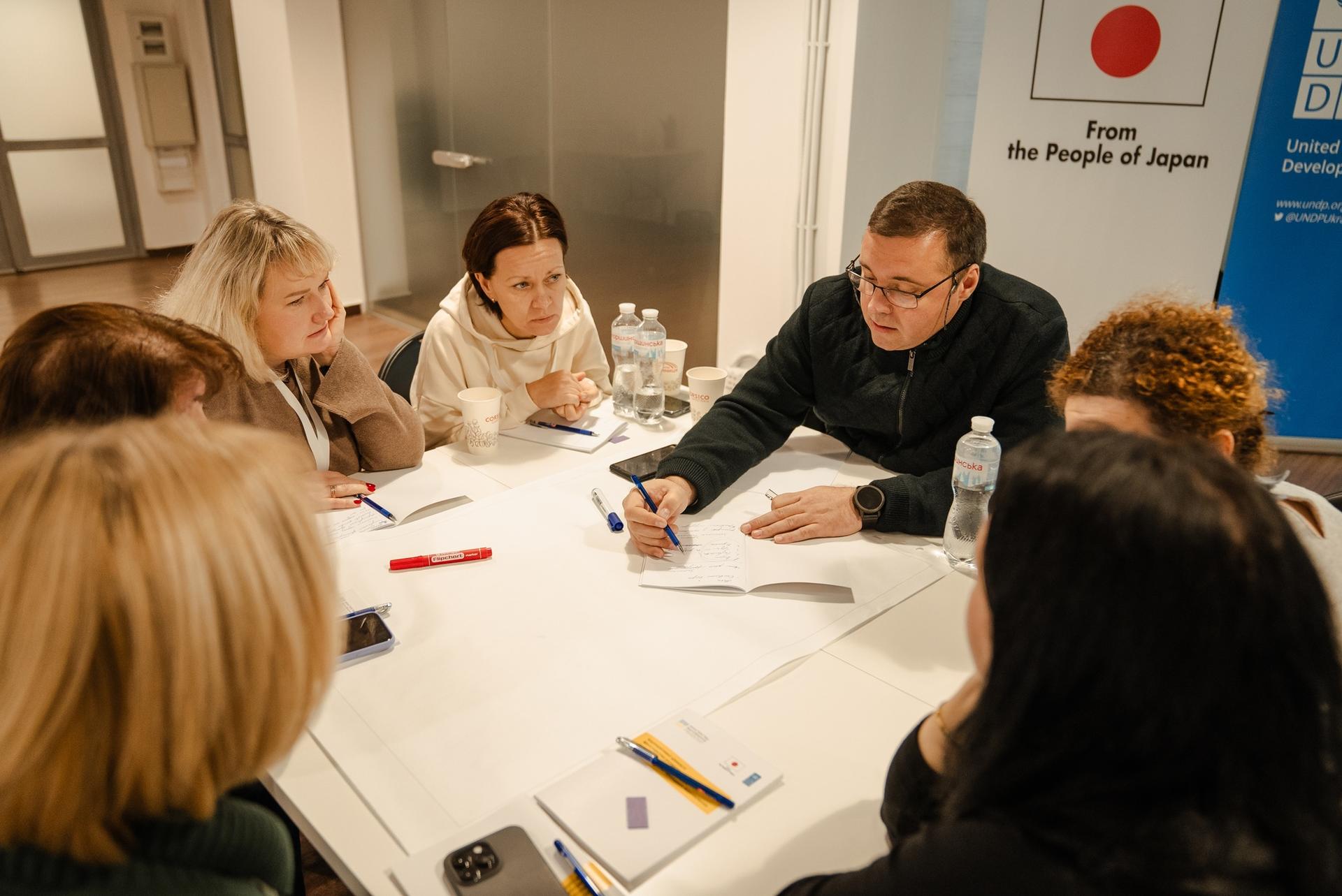 Team around a conference table with papers; a man leads the discussion.