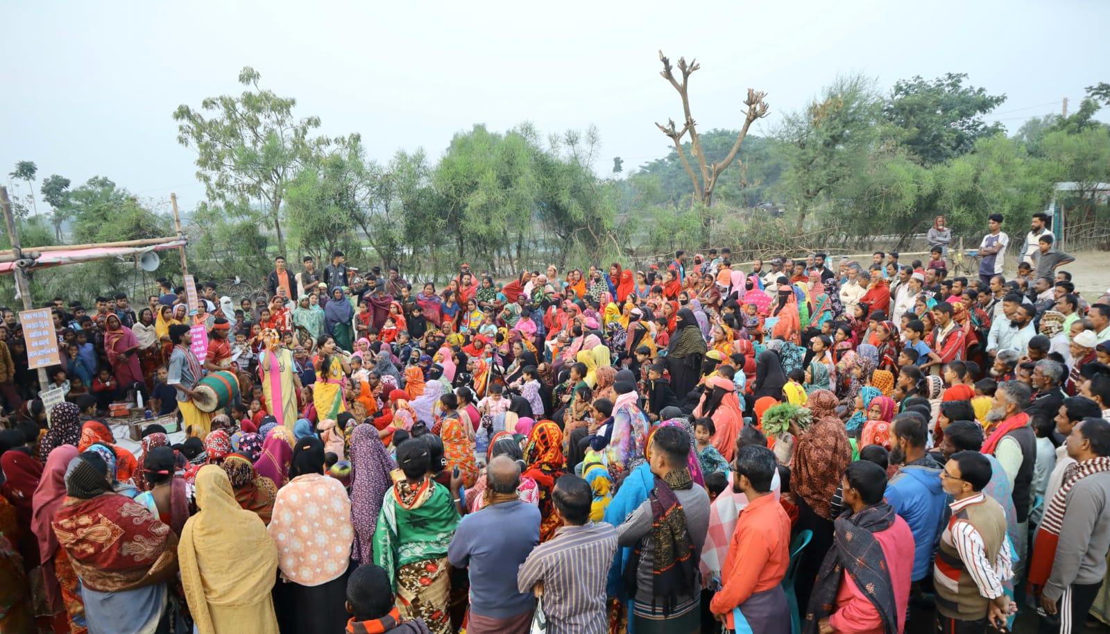 Photograph of a large outdoor crowd at a rural event, colorful clothing, trees in background.