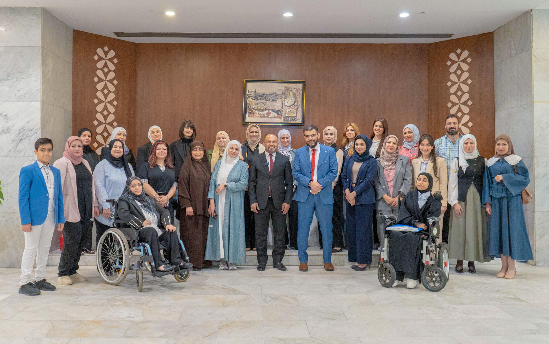 Group photo of diverse adults in a formal hall, two people in wheelchairs at the front.