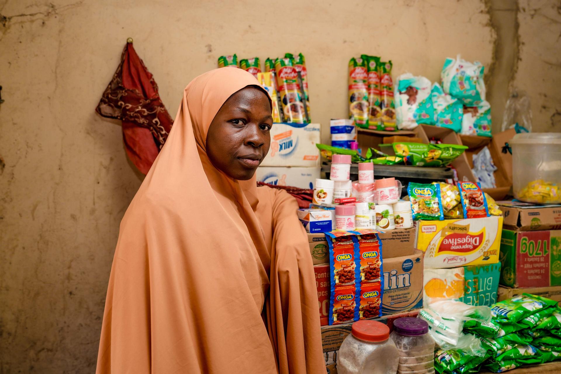 Person in a peach hijab stands in front of a shelf stocked with groceries.