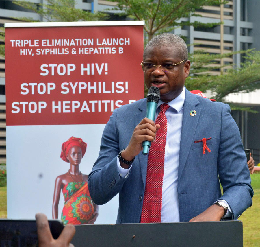 Speaker in a blue blazer at a podium with a banner: Stop HIV, Stop Syphilis, Stop Hepatitis B.