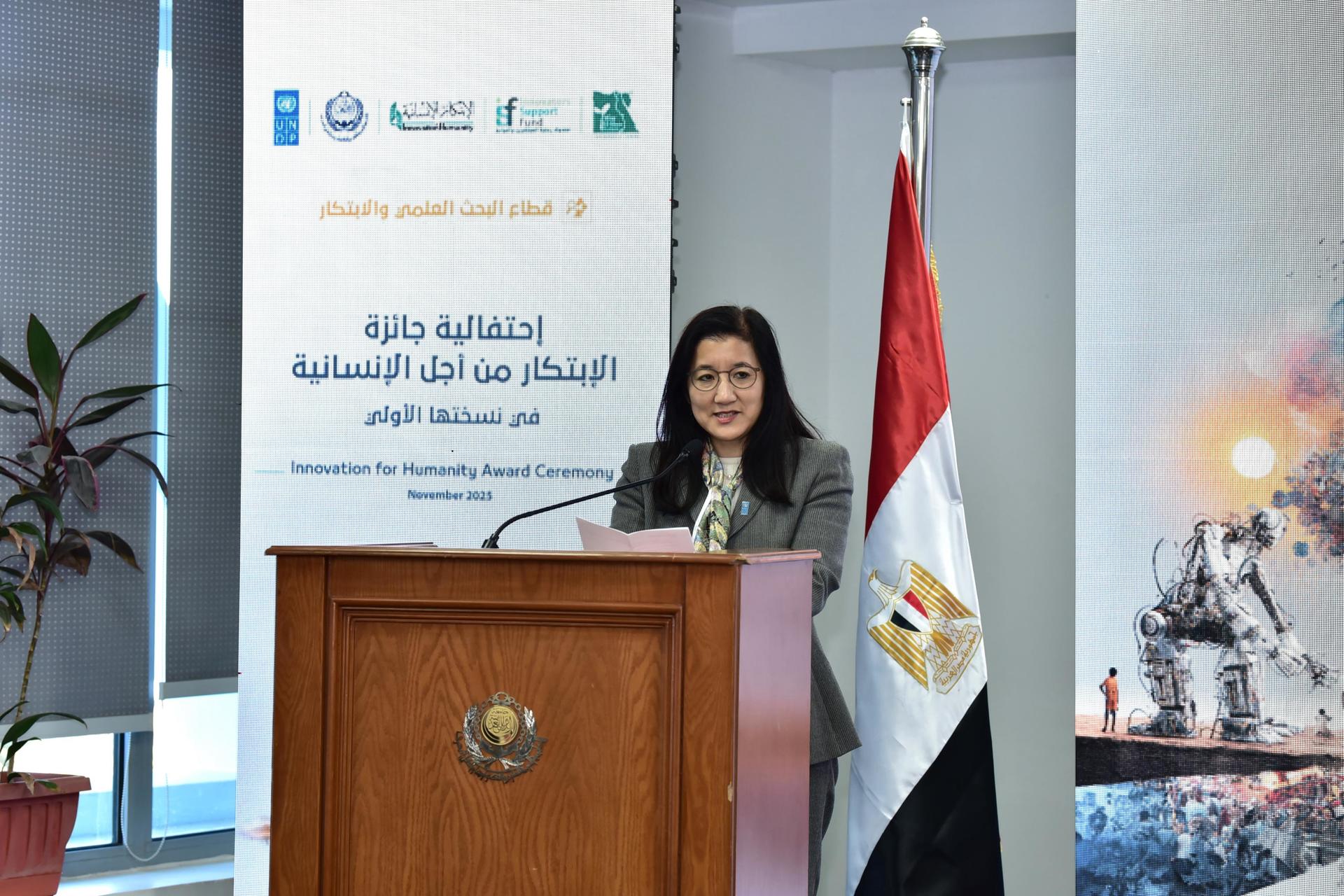 Female speaker at a podium during a formal event, with an Egyptian flag and banner behind.