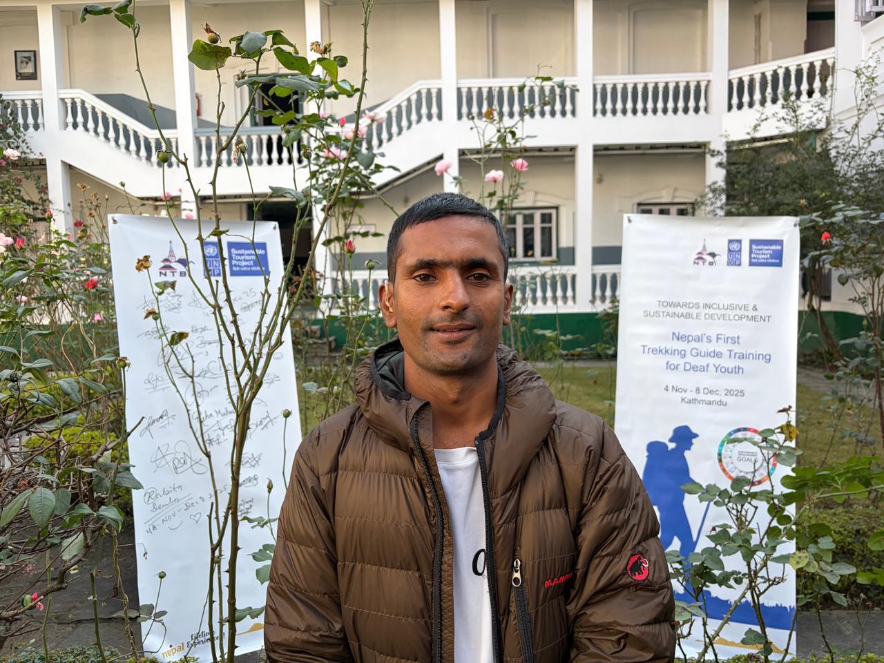 Photograph of a person in brown jacket standing between two banners outdoors, with building behind.